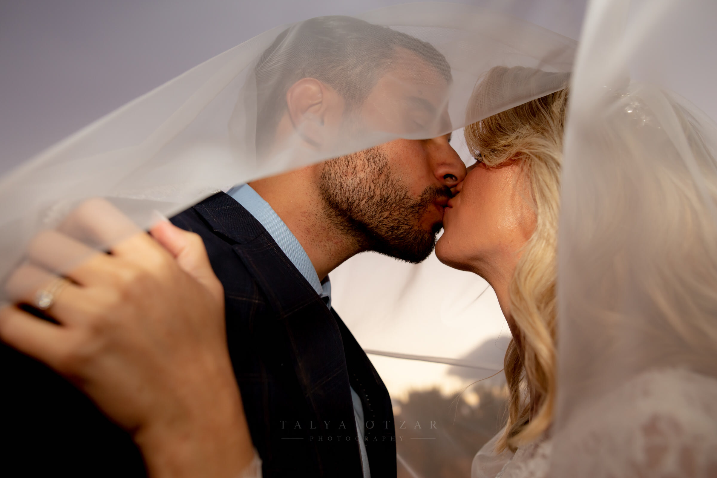 Bride and groom kissing beneath her veil in the last of the light