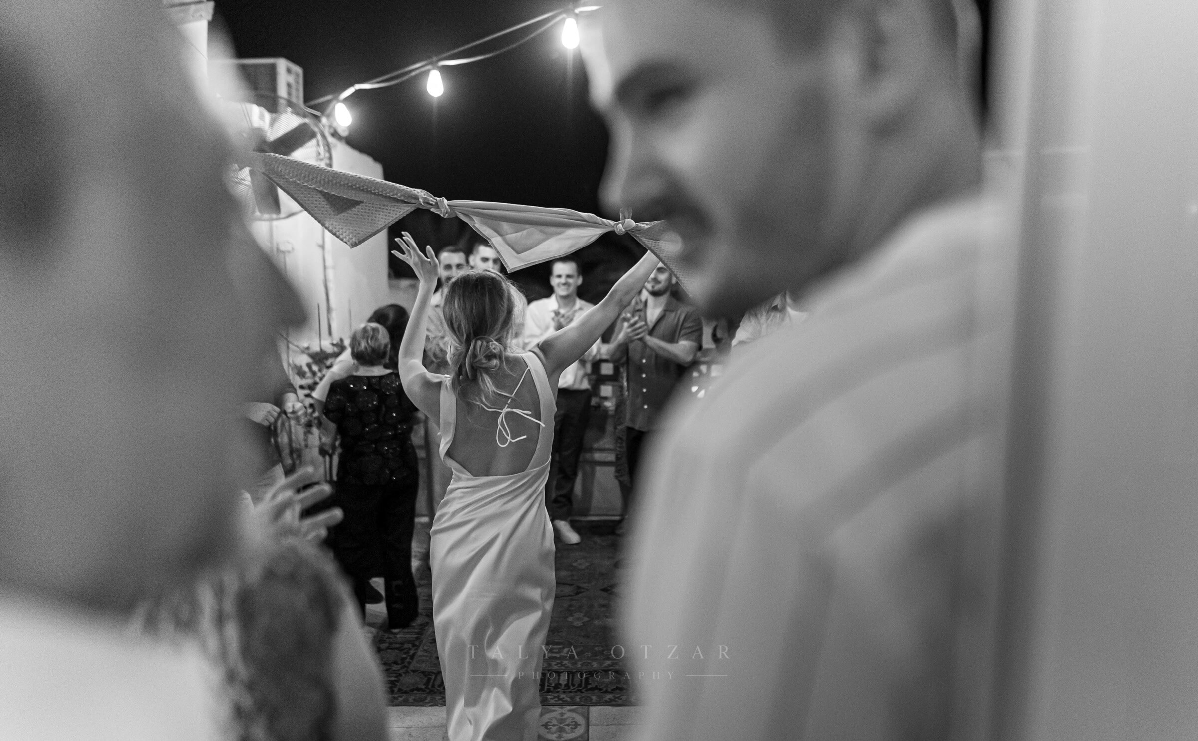 A guest dancing with a scarf raised overhead on the rooftop at night