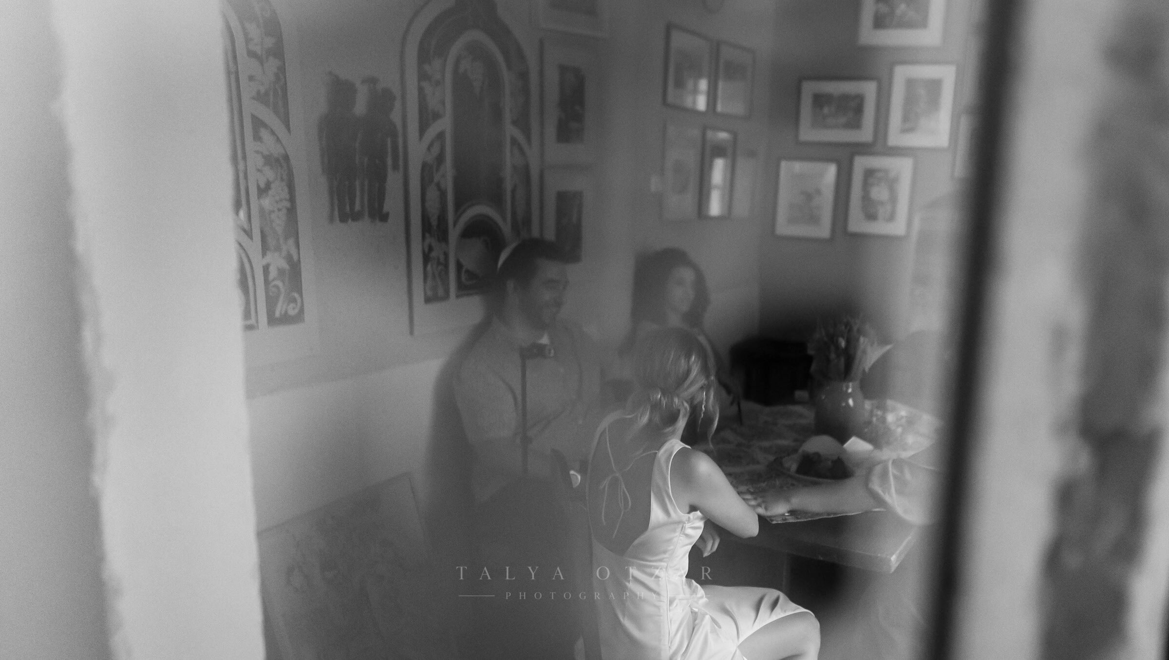 A room hung with picture frames, seen through the doorway as guests talk