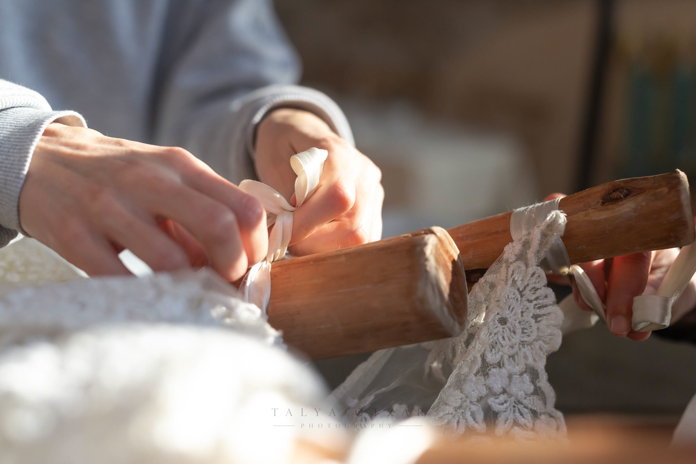Hands tying ribbon and lace around one of the wooden chuppah poles