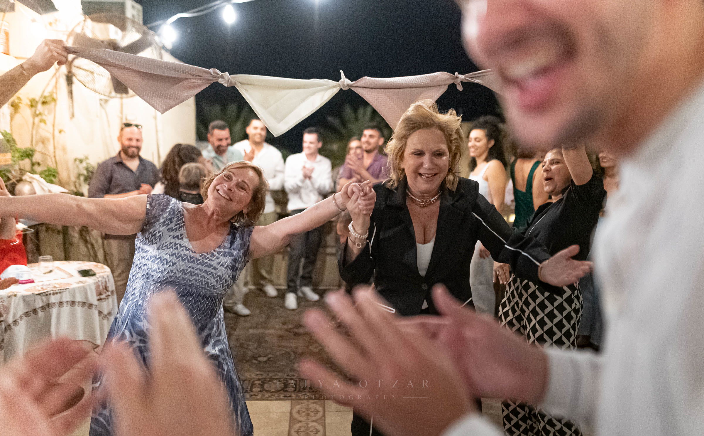 Two women dancing hand in hand at night, guests clapping them on