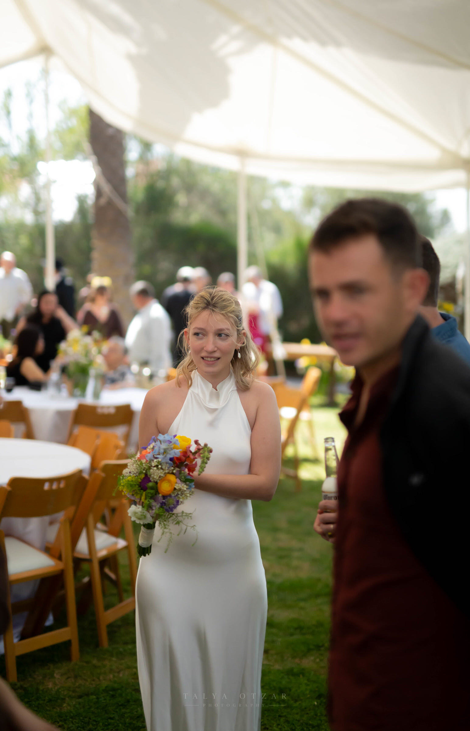 The bride carrying a bouquet of wildflowers through the marquee among the guests