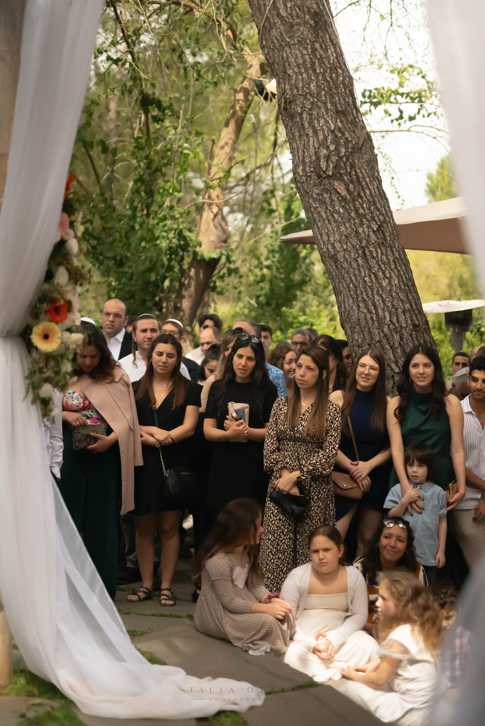 Guests standing among the trees for the ceremony, the bride's train spread across the stone