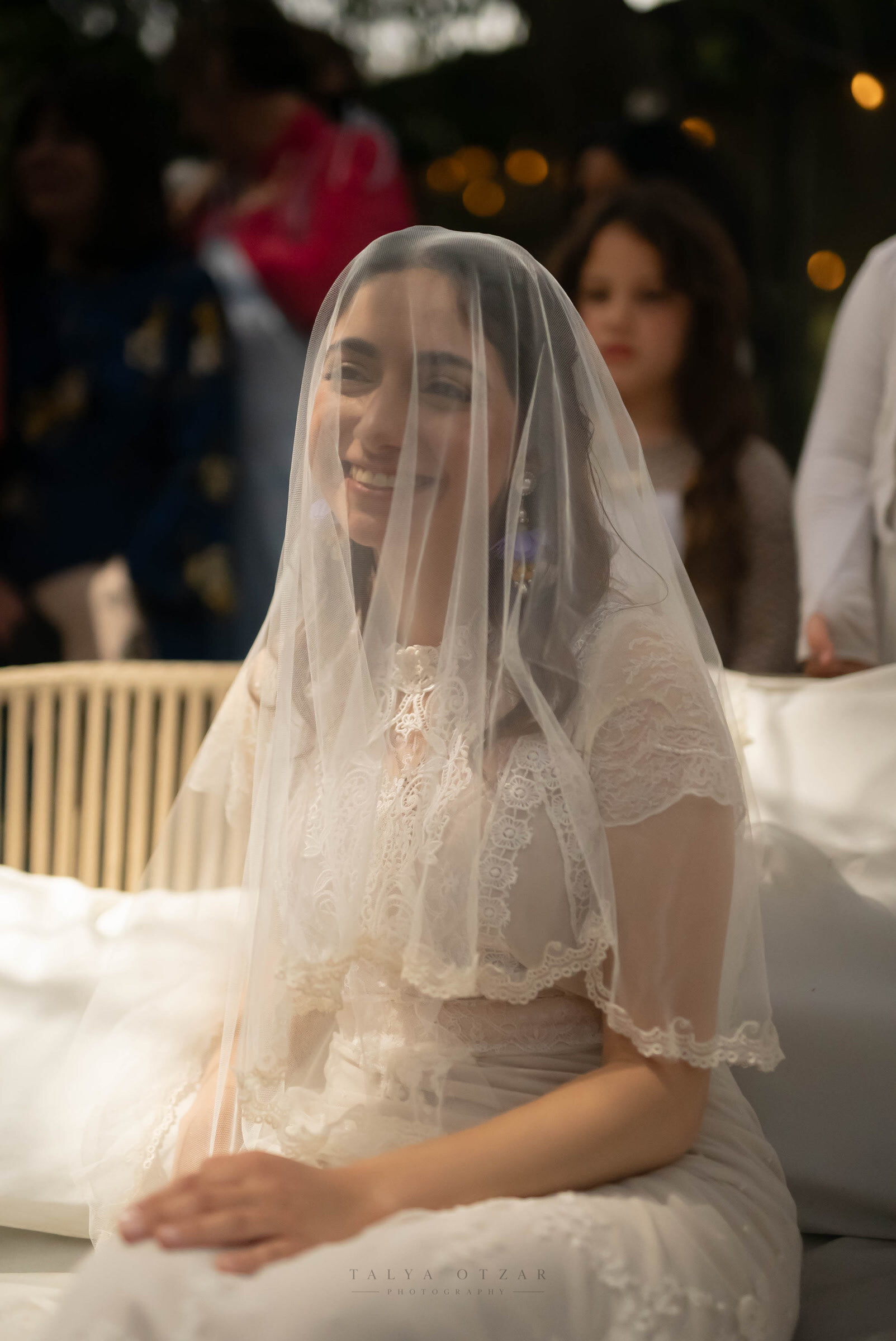 The bride smiling beneath her lace veil while she waits for the ceremony to begin