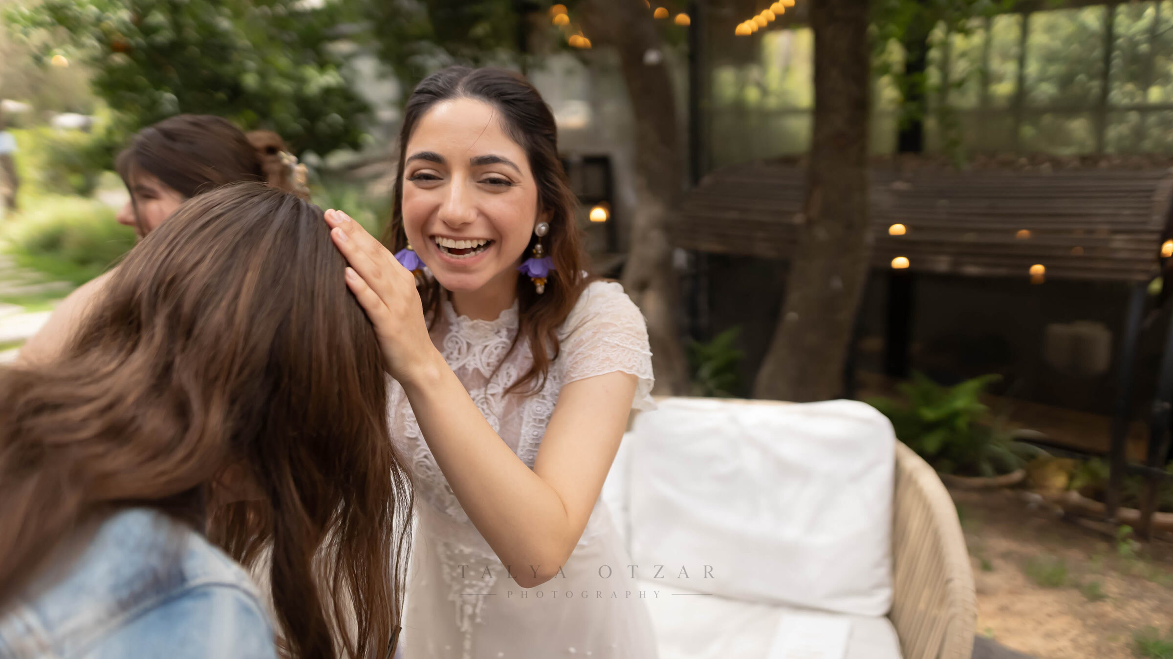 The bride laughing as she reaches out to a friend, garden lights strung behind