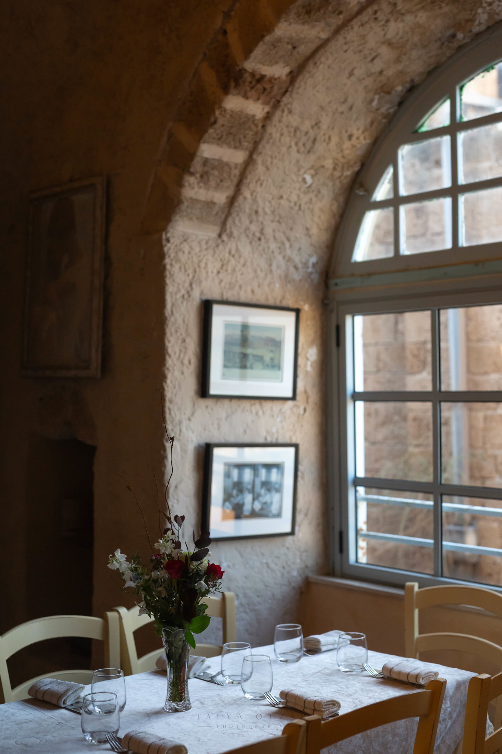 A table laid beneath the vaulted stone ceiling, framed photographs on the wall and roses in a vase