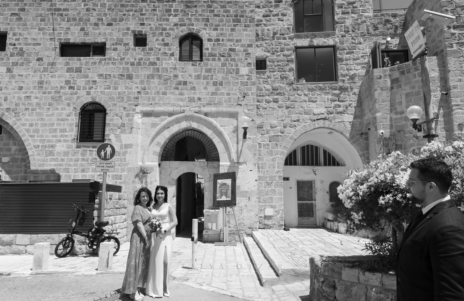 The bride and a friend in a Jaffa stone alley, the groom waiting in the foreground