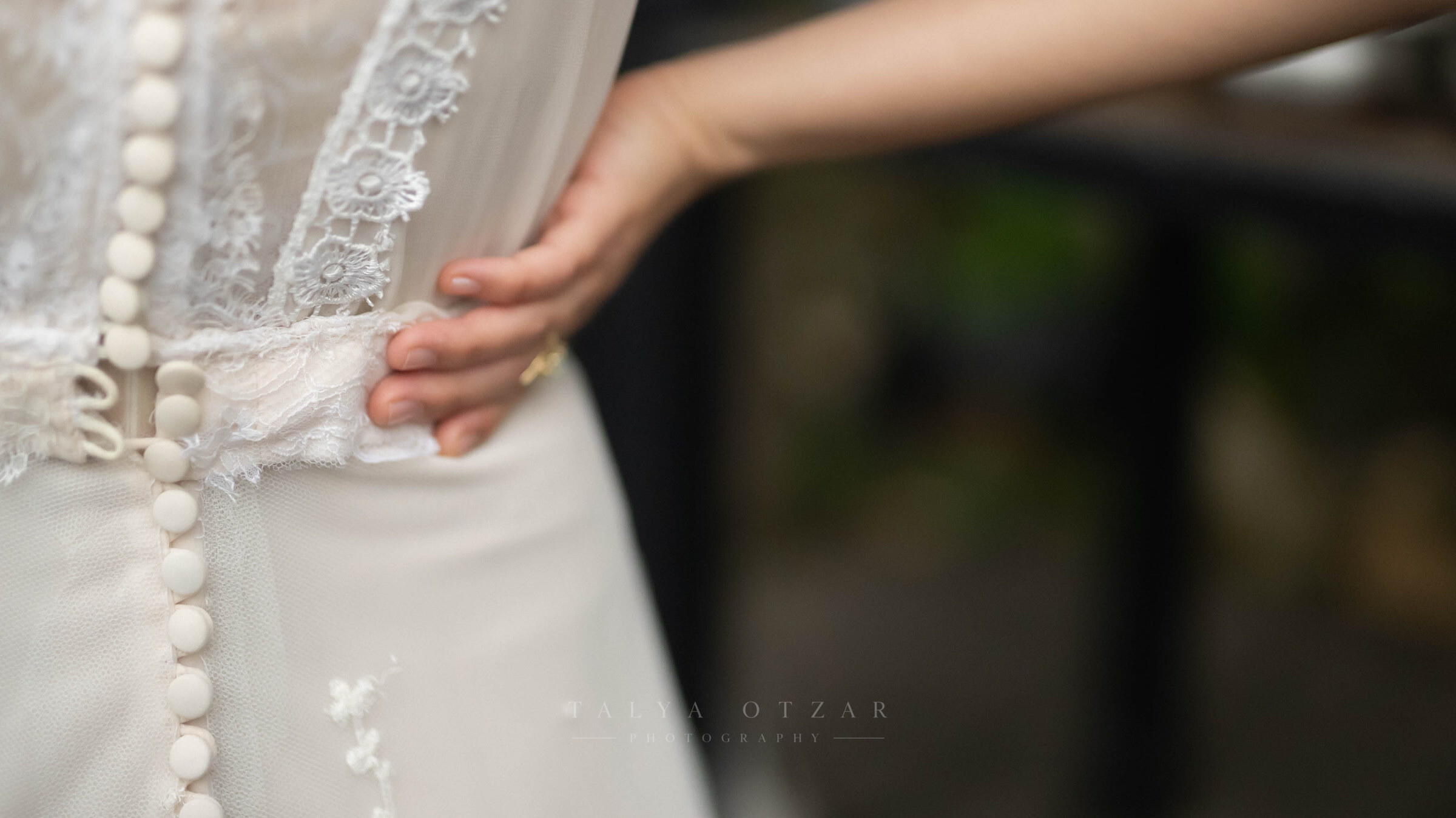 A hand resting on the lace and buttoned back of the wedding dress