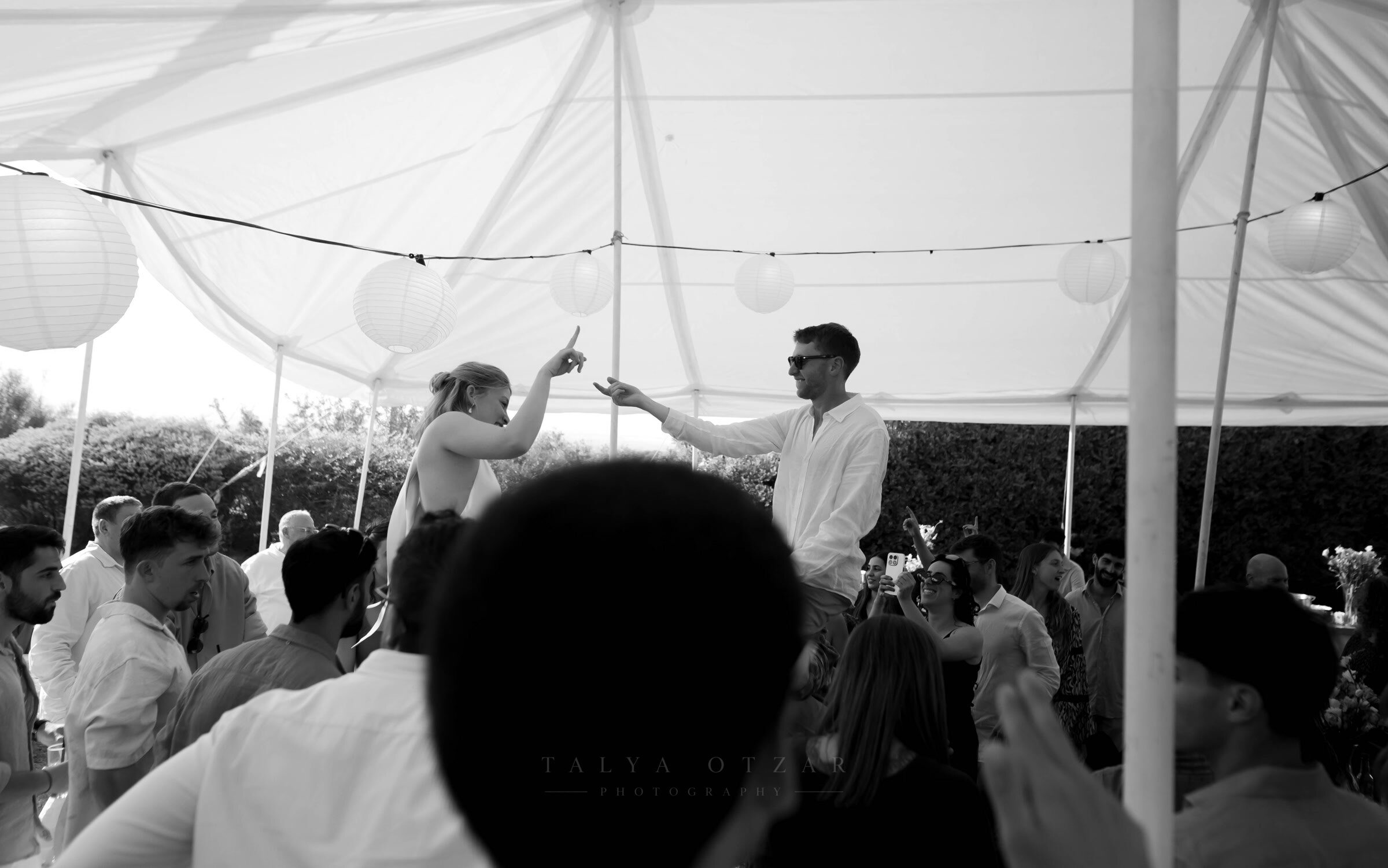 Bride and groom lifted on chairs beneath the marquee, reaching towards each other