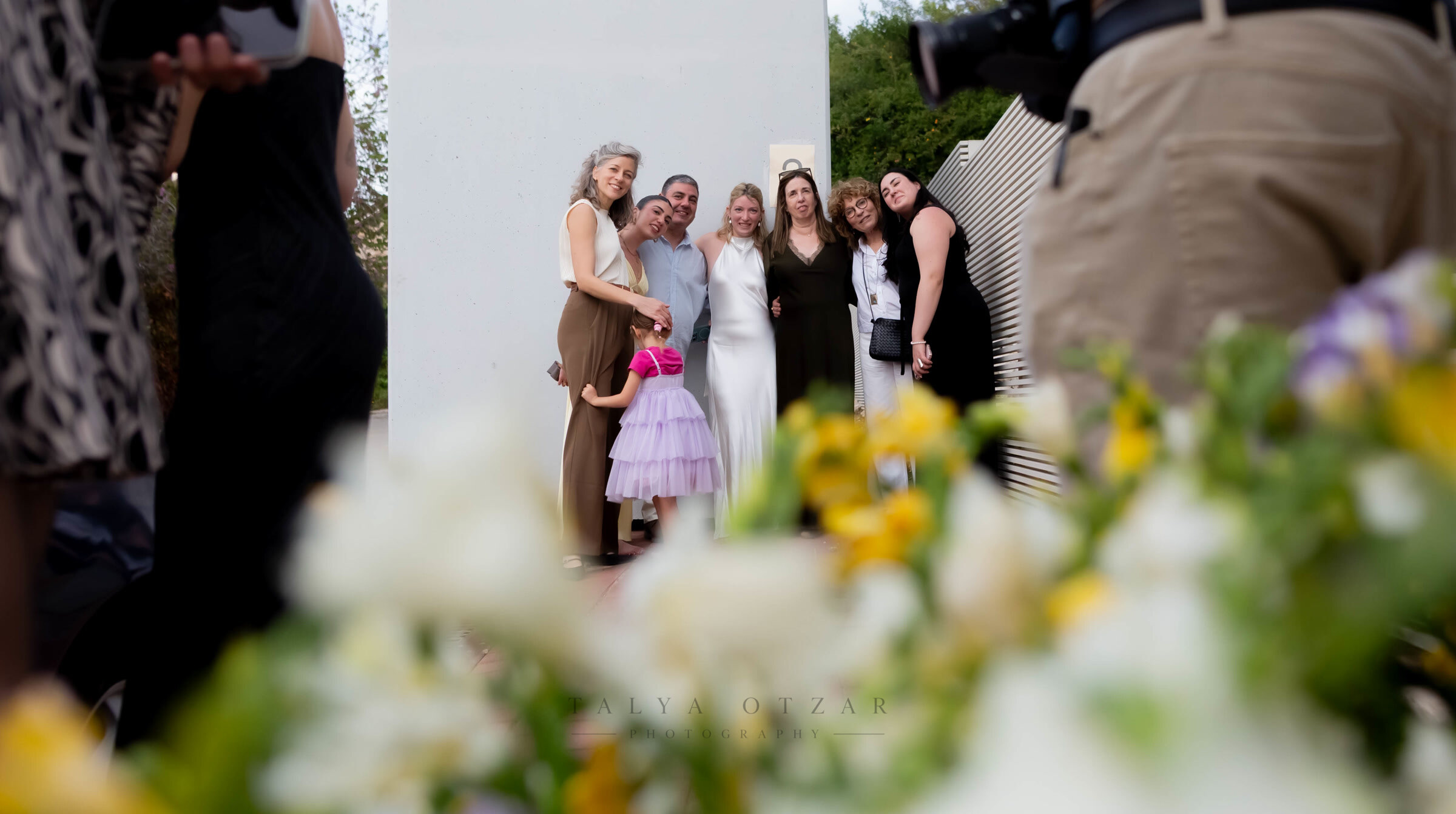 Guests gathering for a group photograph, seen past a foreground of yellow and white flowers