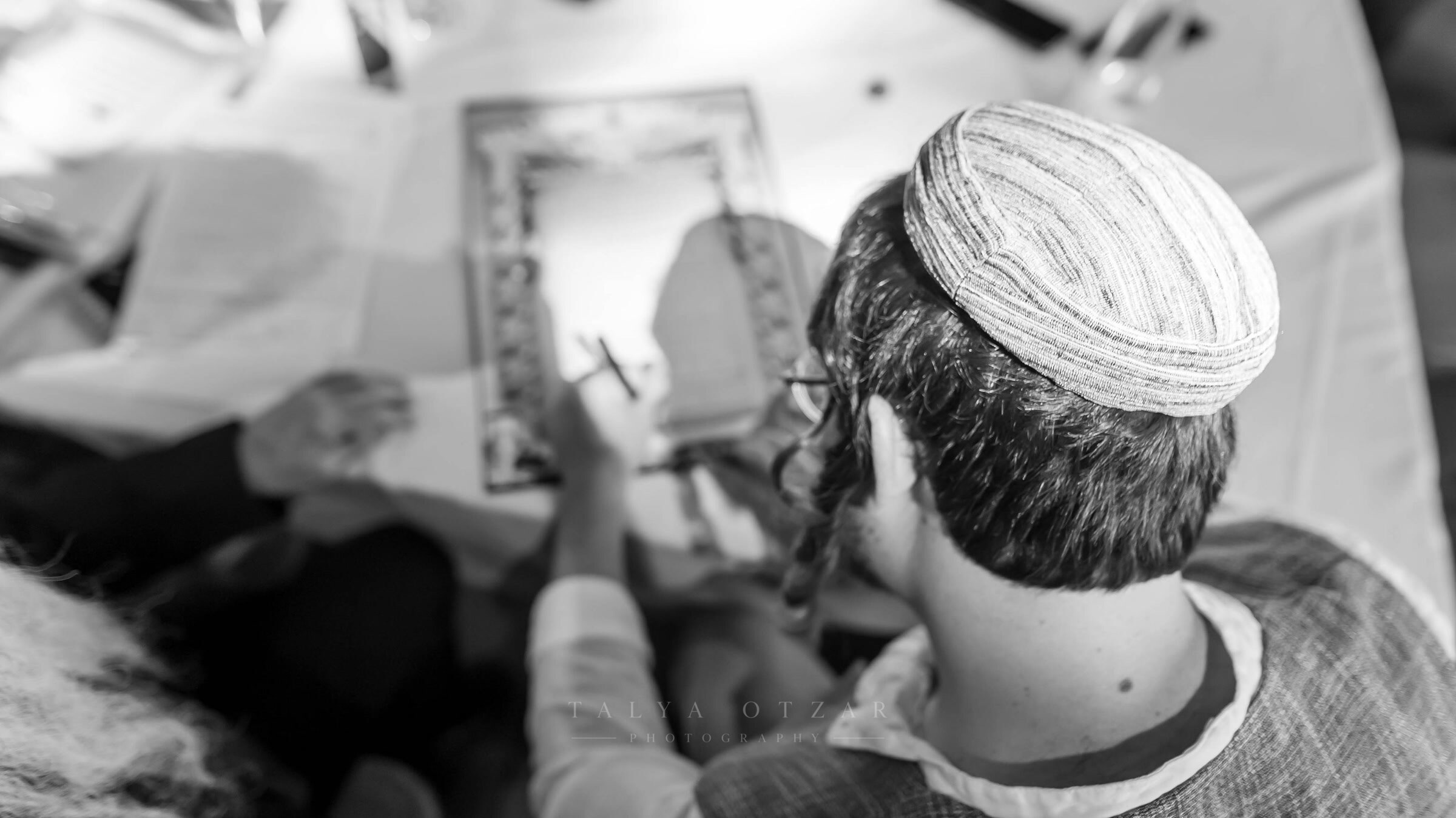 Signing the ketubah, photographed from above over the groom's shoulder
