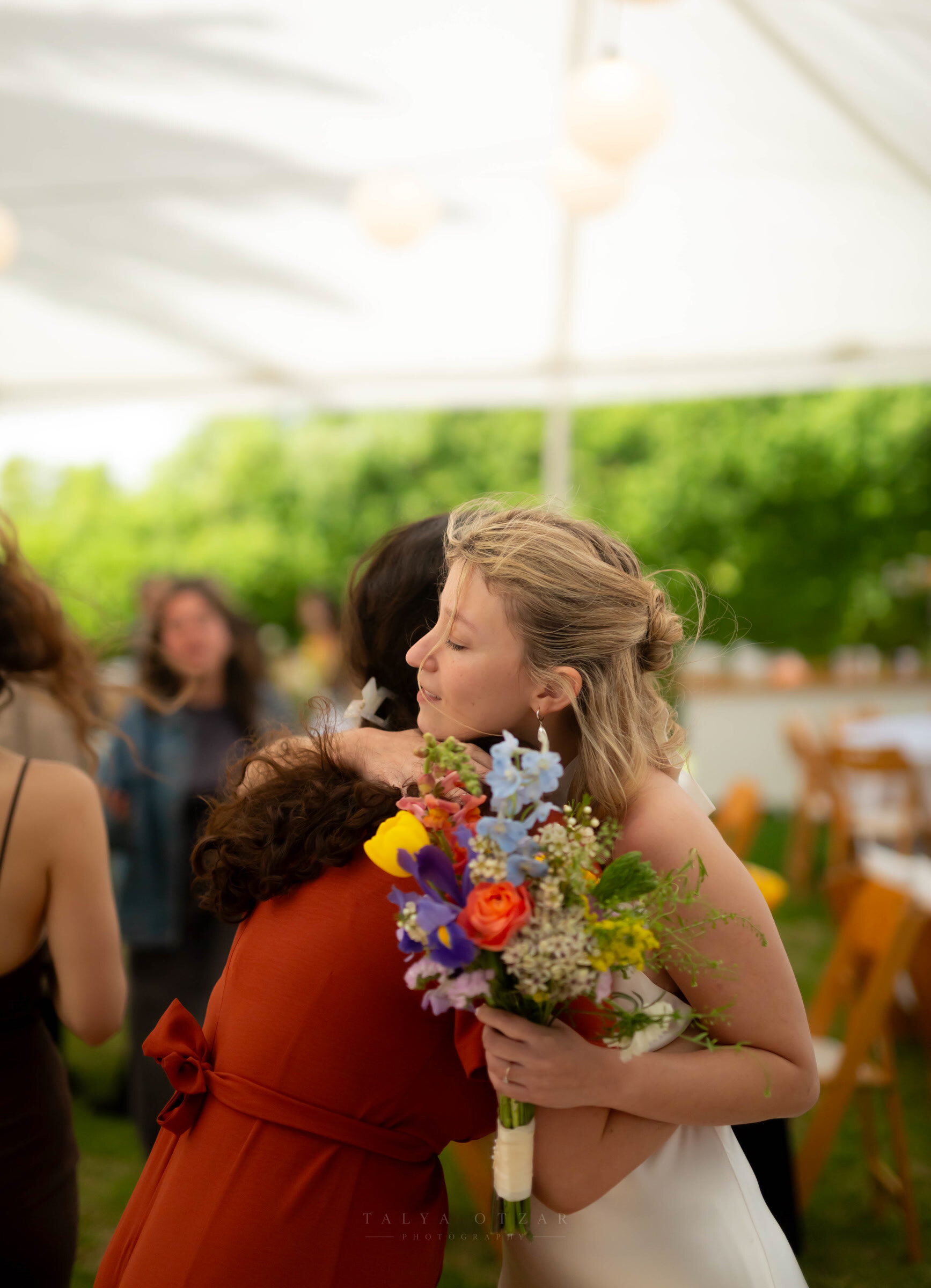 The bride holding a guest in a long hug, her wildflower bouquet between them