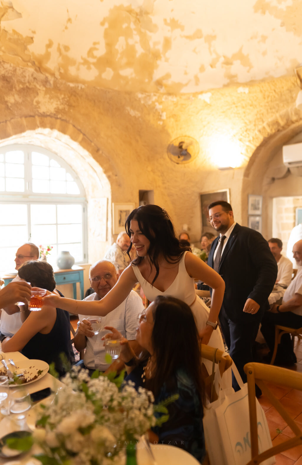The bride reaching across the table to raise a glass with her guests