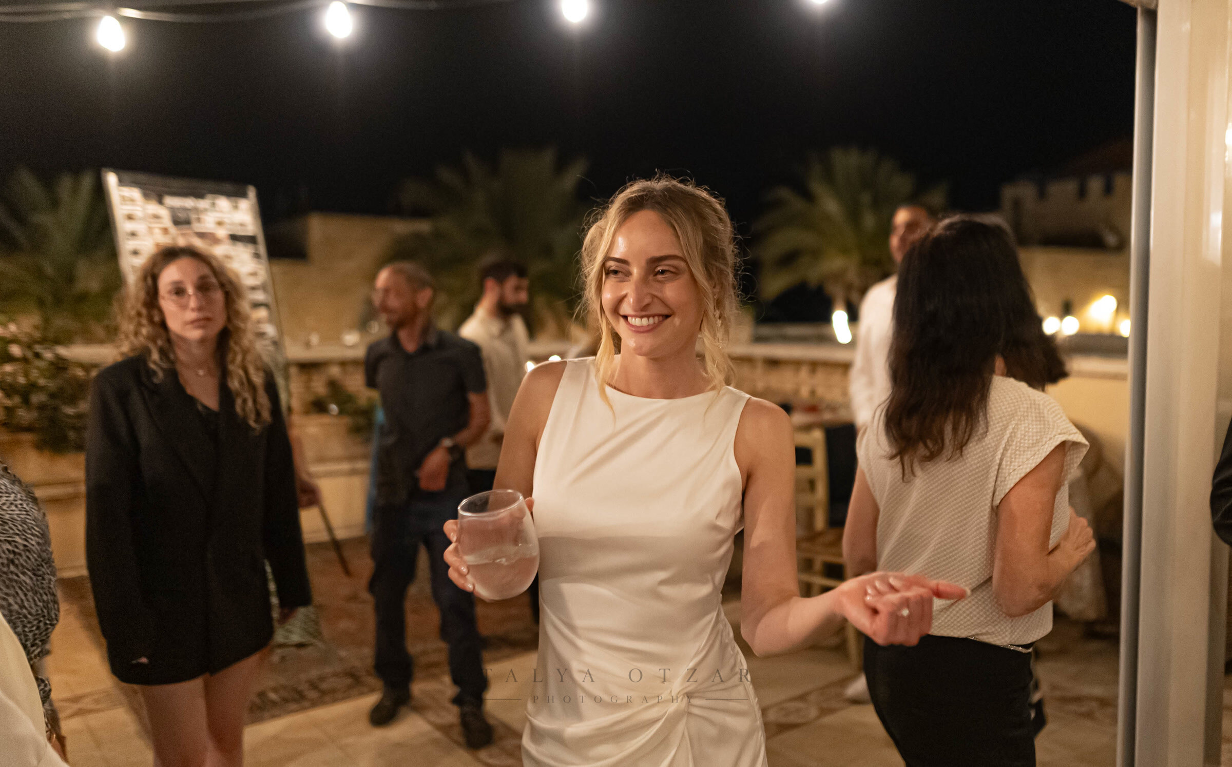 The bride with a drink in hand at the evening reception on the rooftop