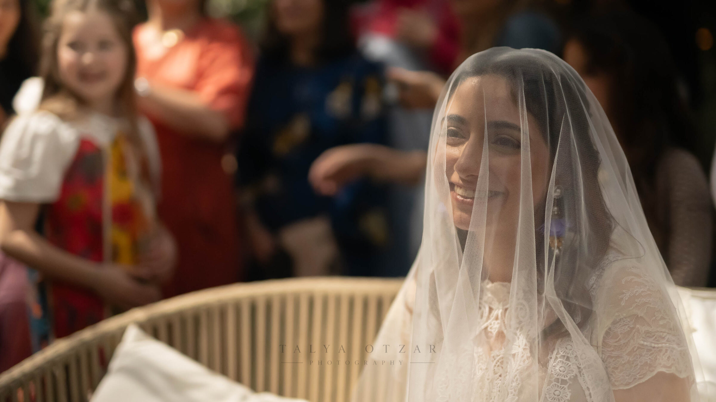 The bride smiling under her veil, children watching from behind her chair