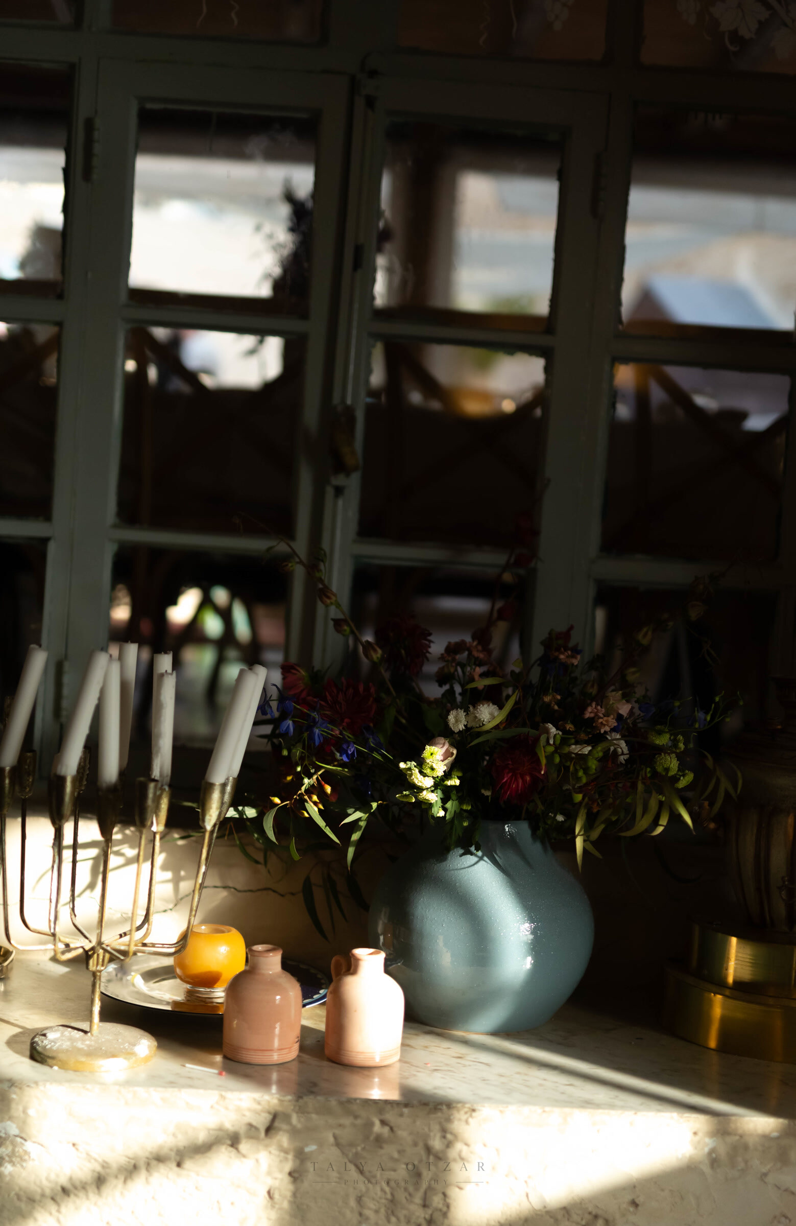 Brass candlesticks and a jug of dark wildflowers on a sunlit stone sill