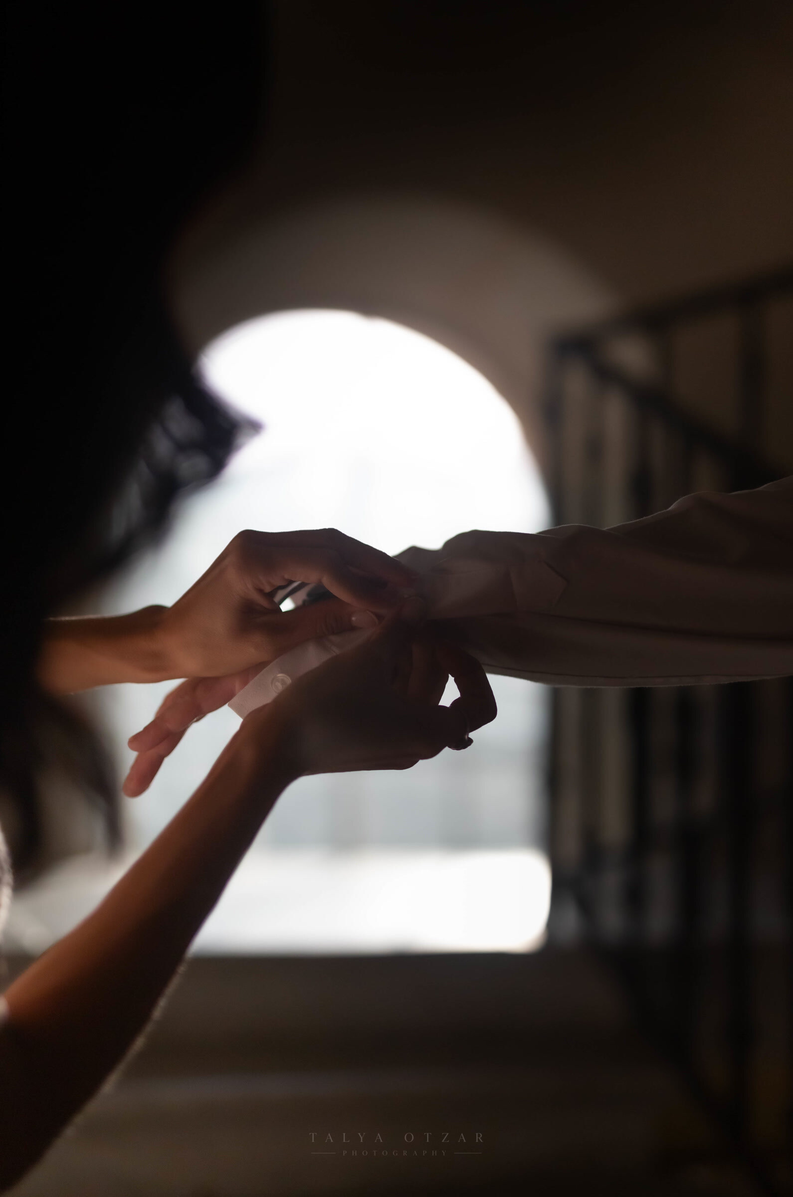 Backlit hands fastening a cuff in the light of the arched window