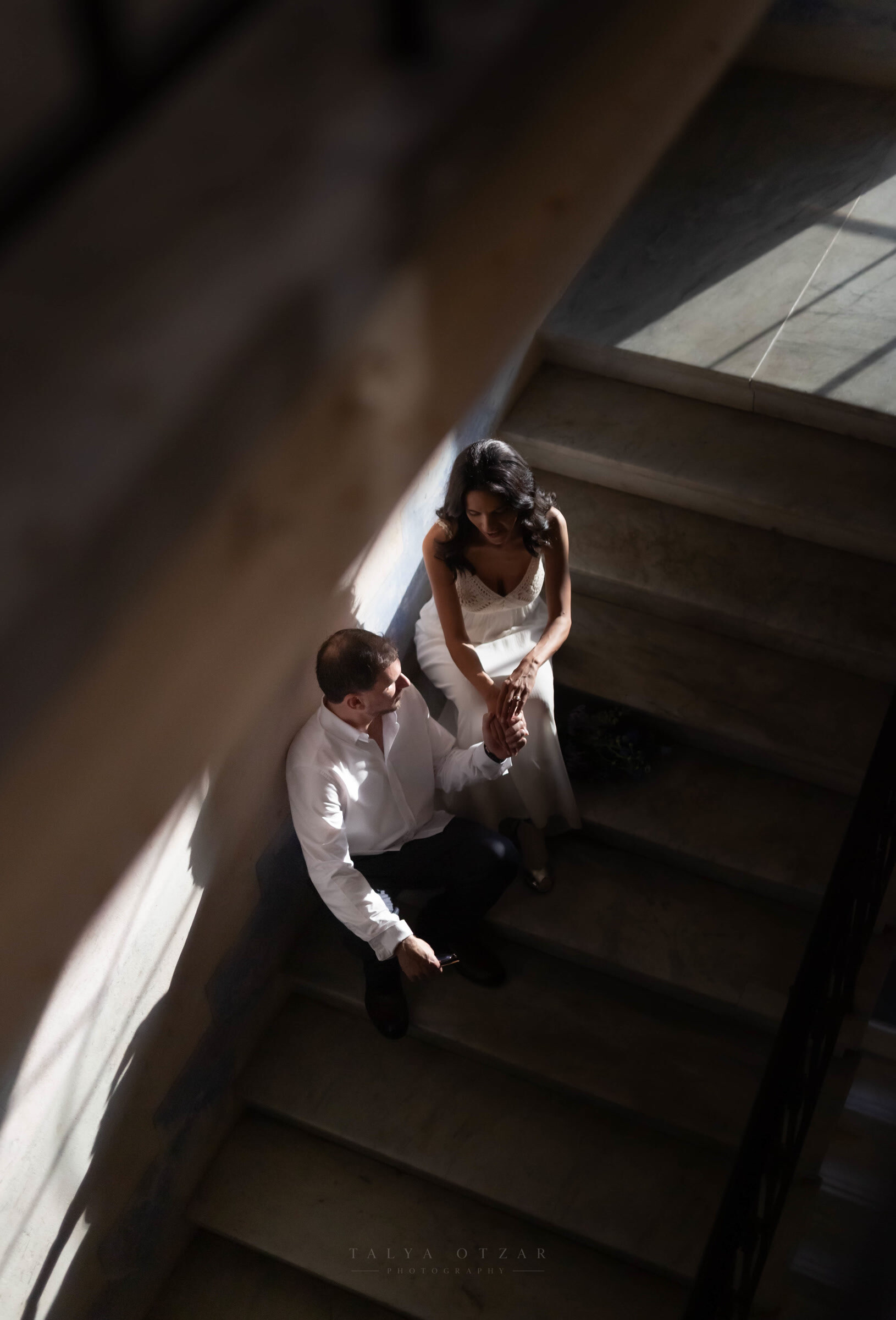 The couple sitting on the stone staircase in the light, hands held between them