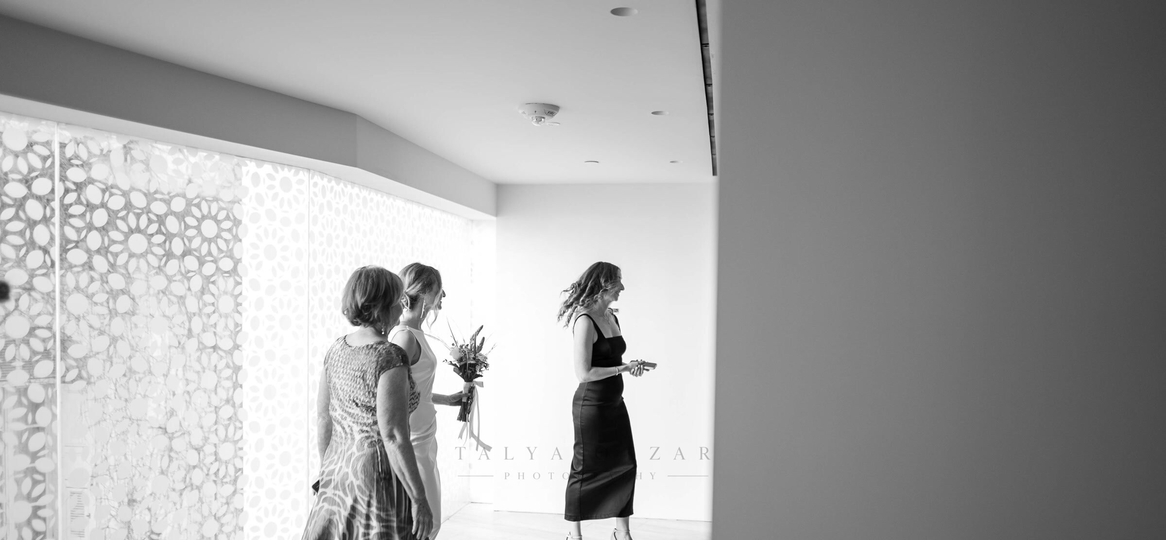 Three women walking the corridor together, one carrying the bouquet