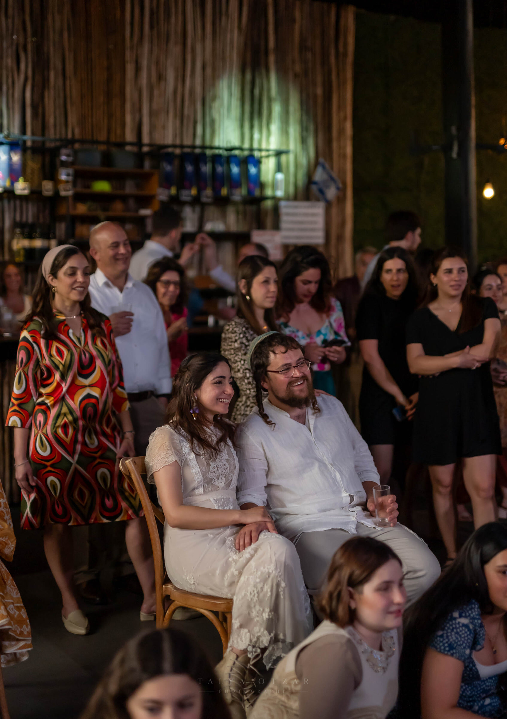 Bride and groom seated among the guests, laughing at something off to the side
