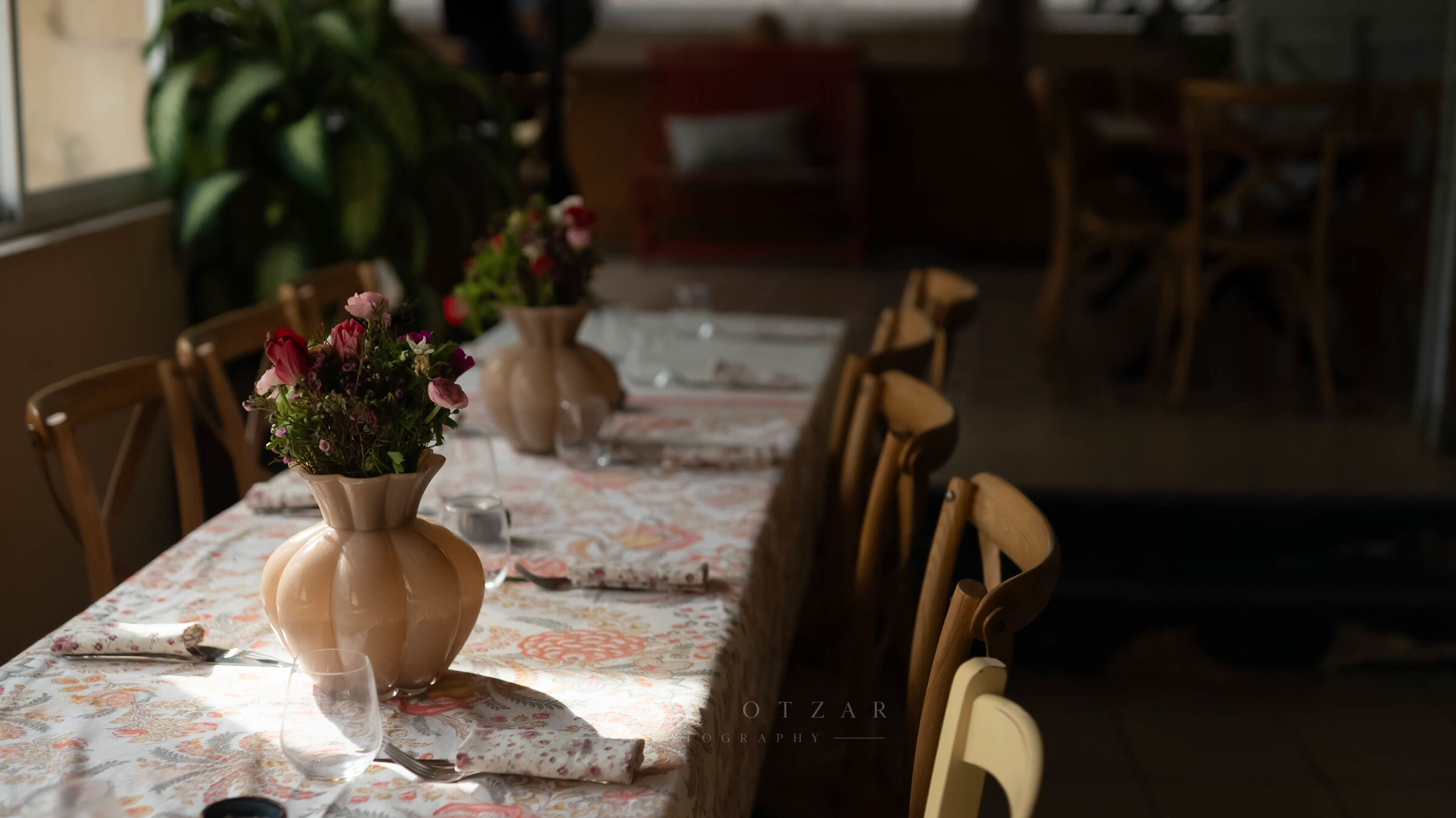 The table laid with a patterned cloth and pink flowers, sunlight falling across it