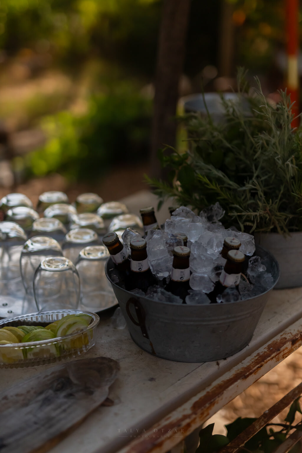 Bottled drinks on ice in a galvanised tub beside upturned glasses and sliced lime