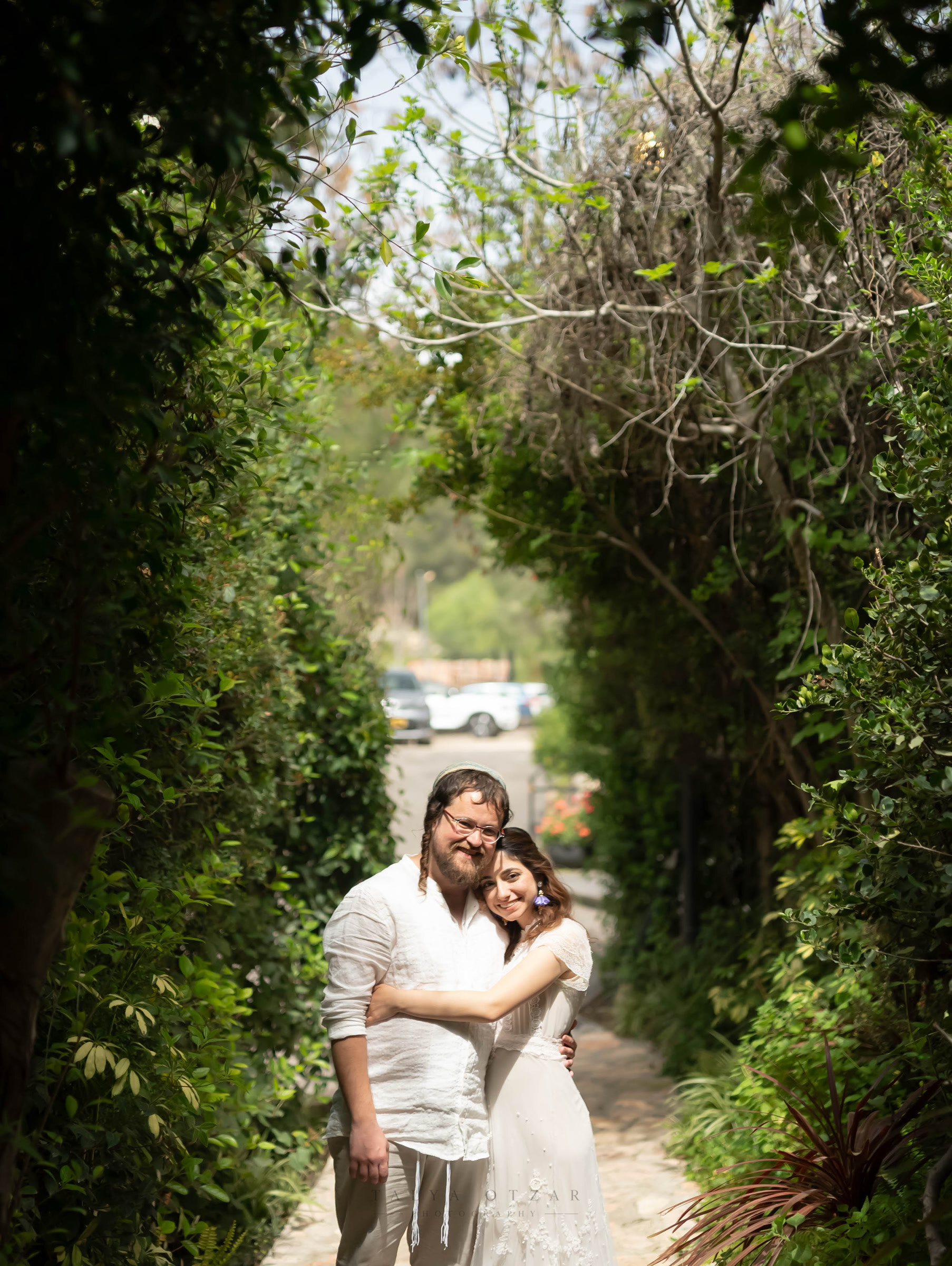 The couple holding each other on a garden path arched over with green