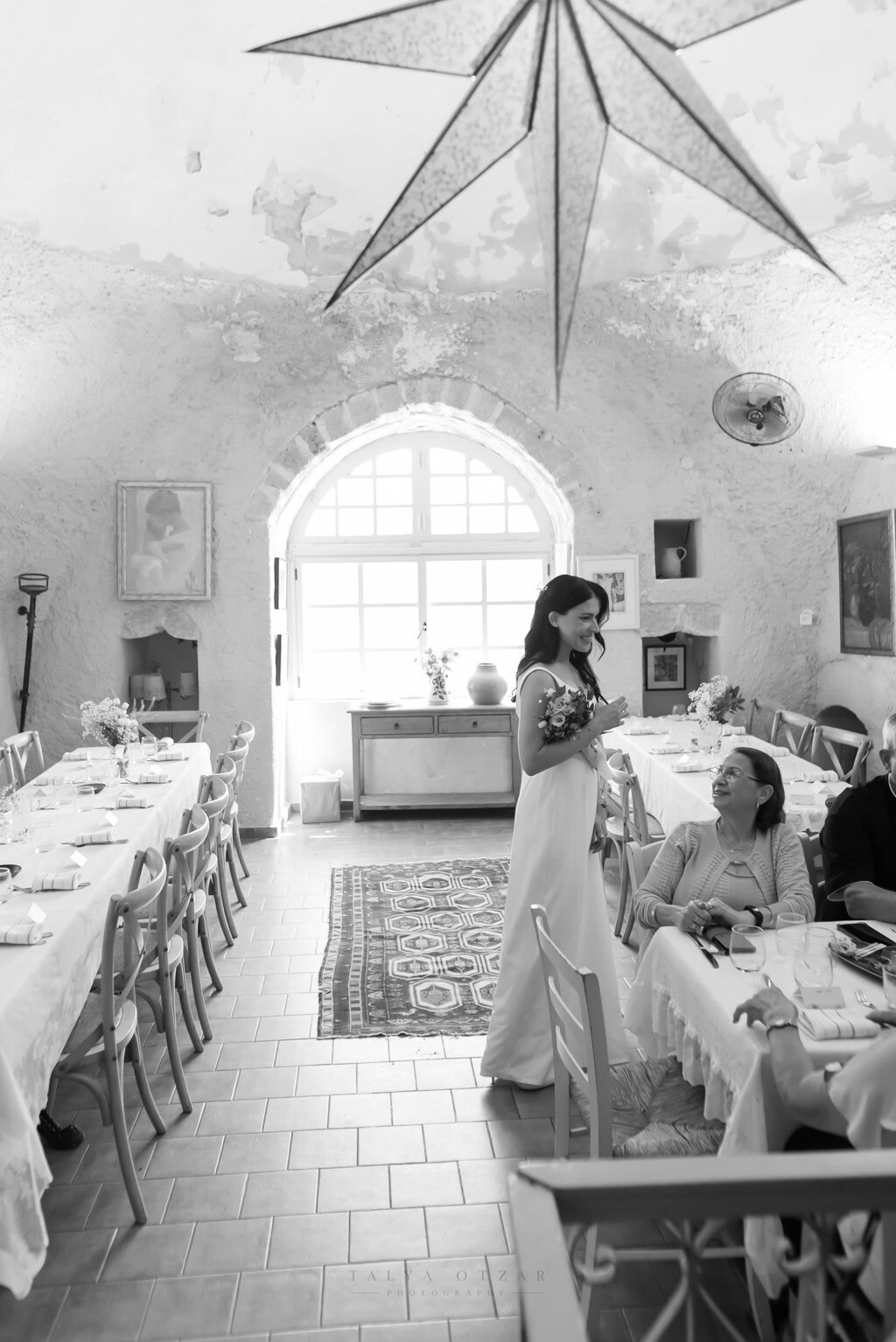 The bride walking through the vaulted dining room with her bouquet, a paper star hanging above