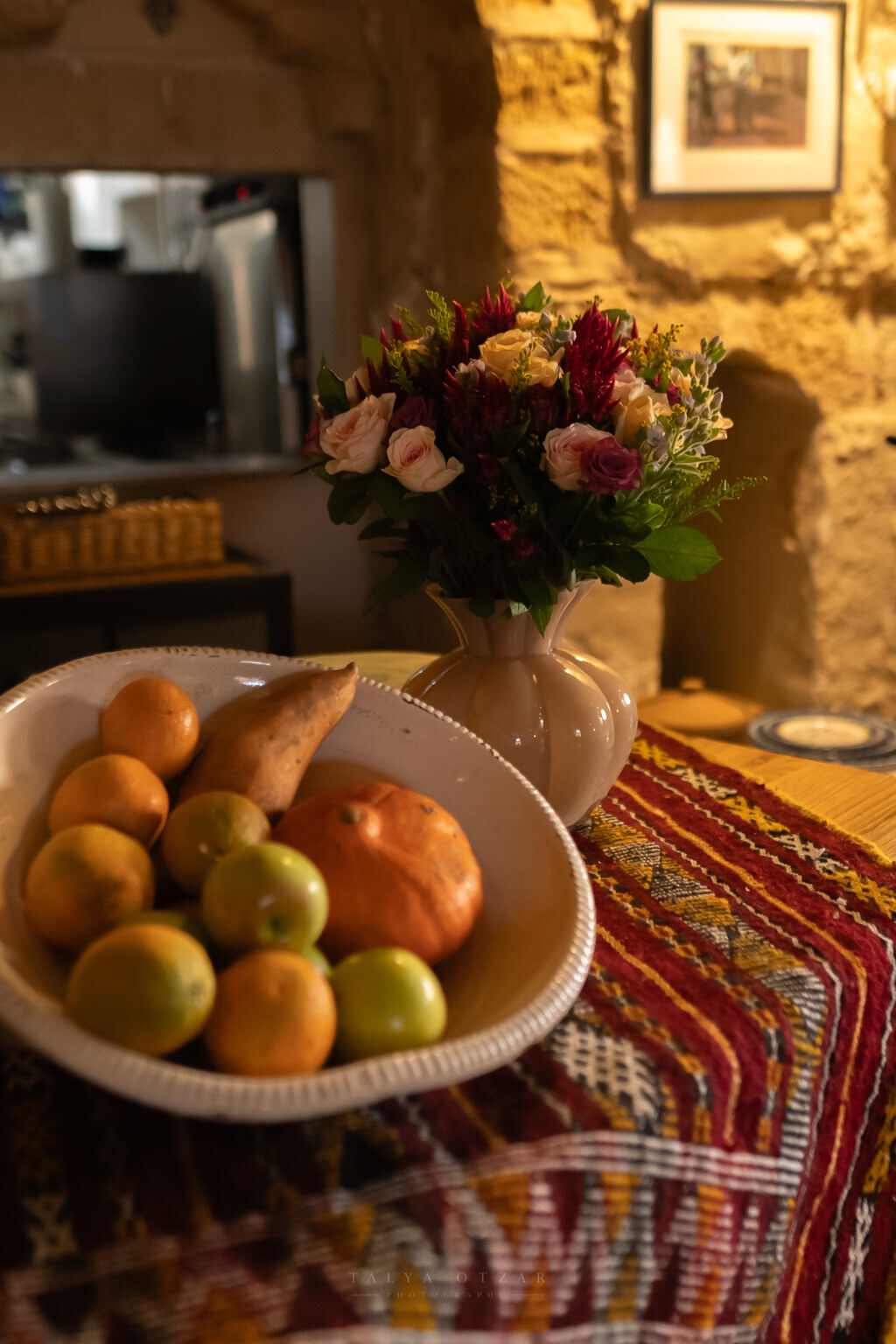 A bowl of citrus and a vase of roses on a woven runner in the warm stone room