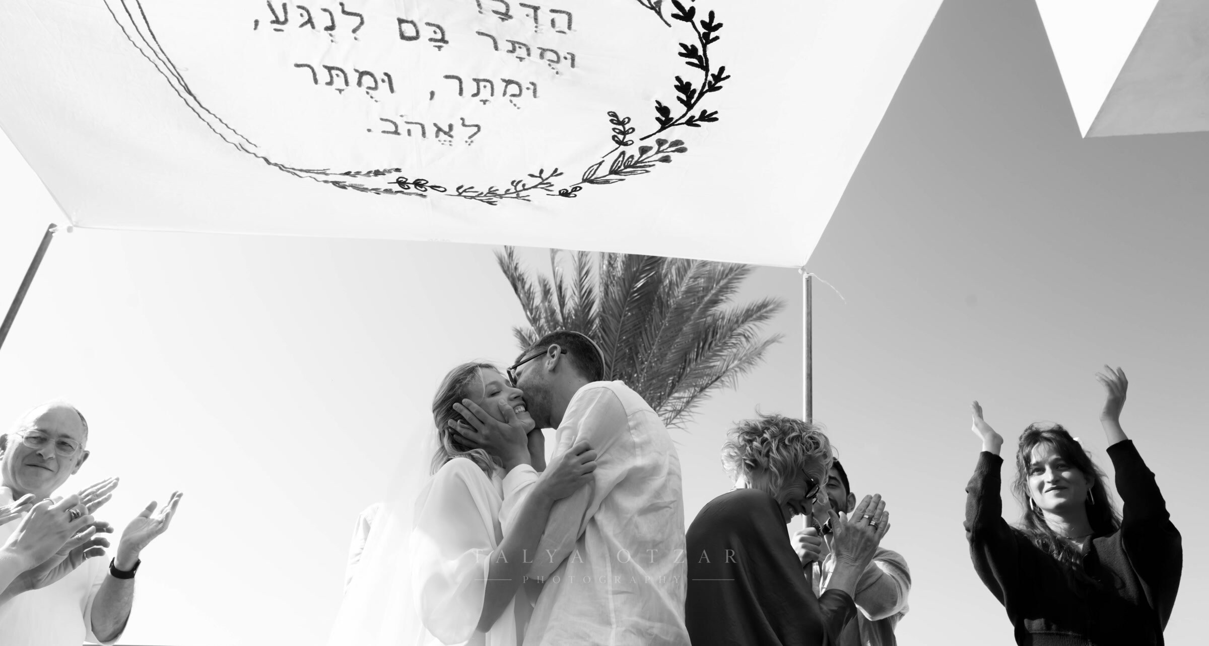 The couple's first kiss under the embroidered chuppah as the guests applaud