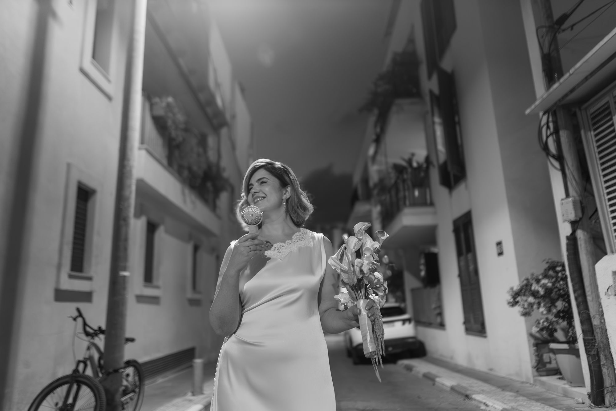 The bride laughing in a quiet street, holding her bouquet, black and white