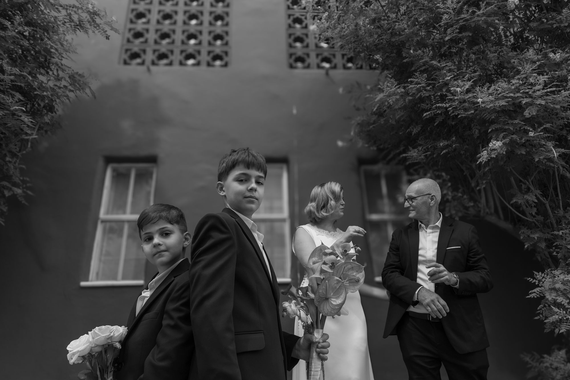 The two boys in suits in front, the couple laughing behind them, black and white