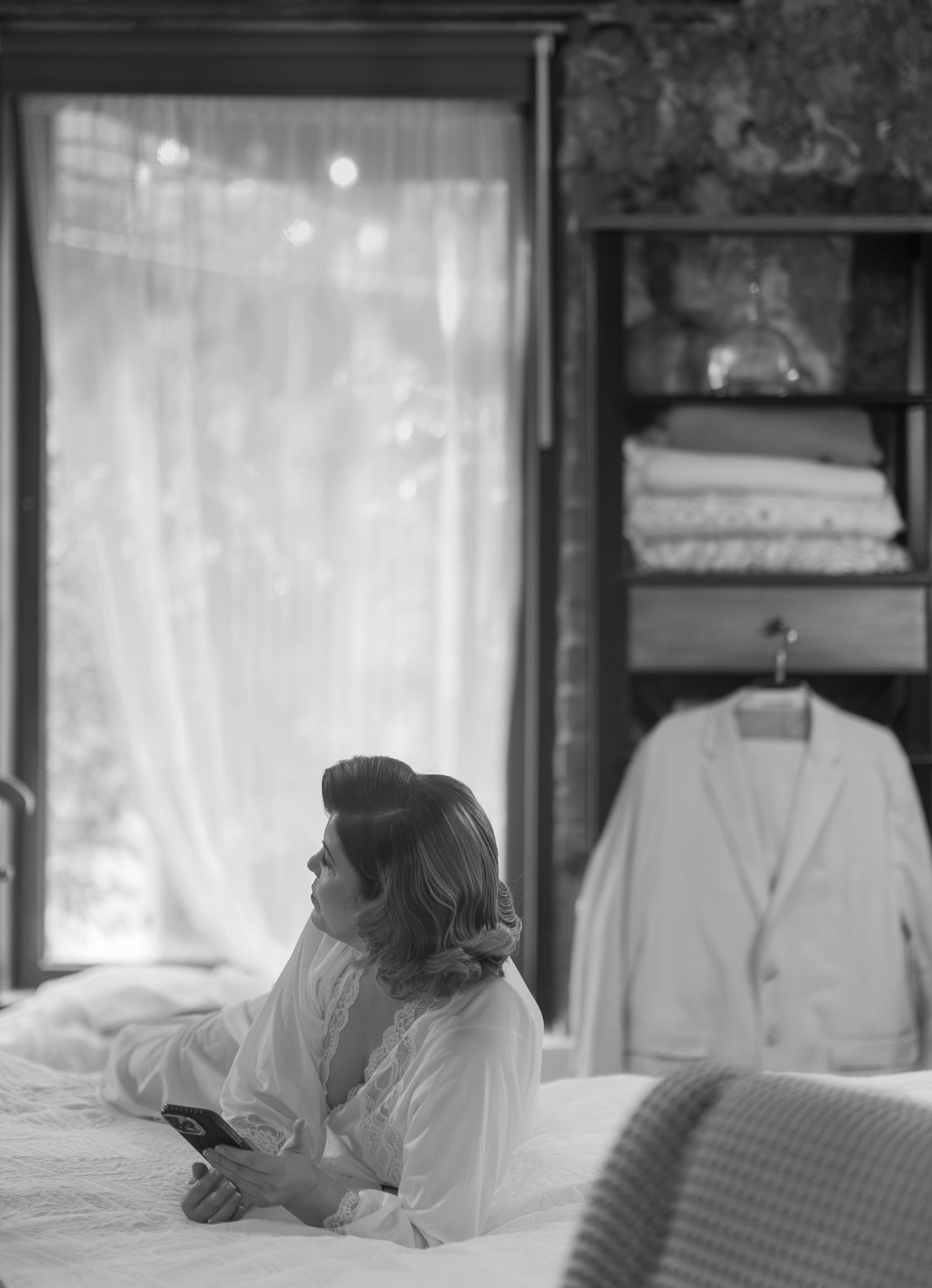 The bride lying on the bed in her robe, looking toward the window, black and white