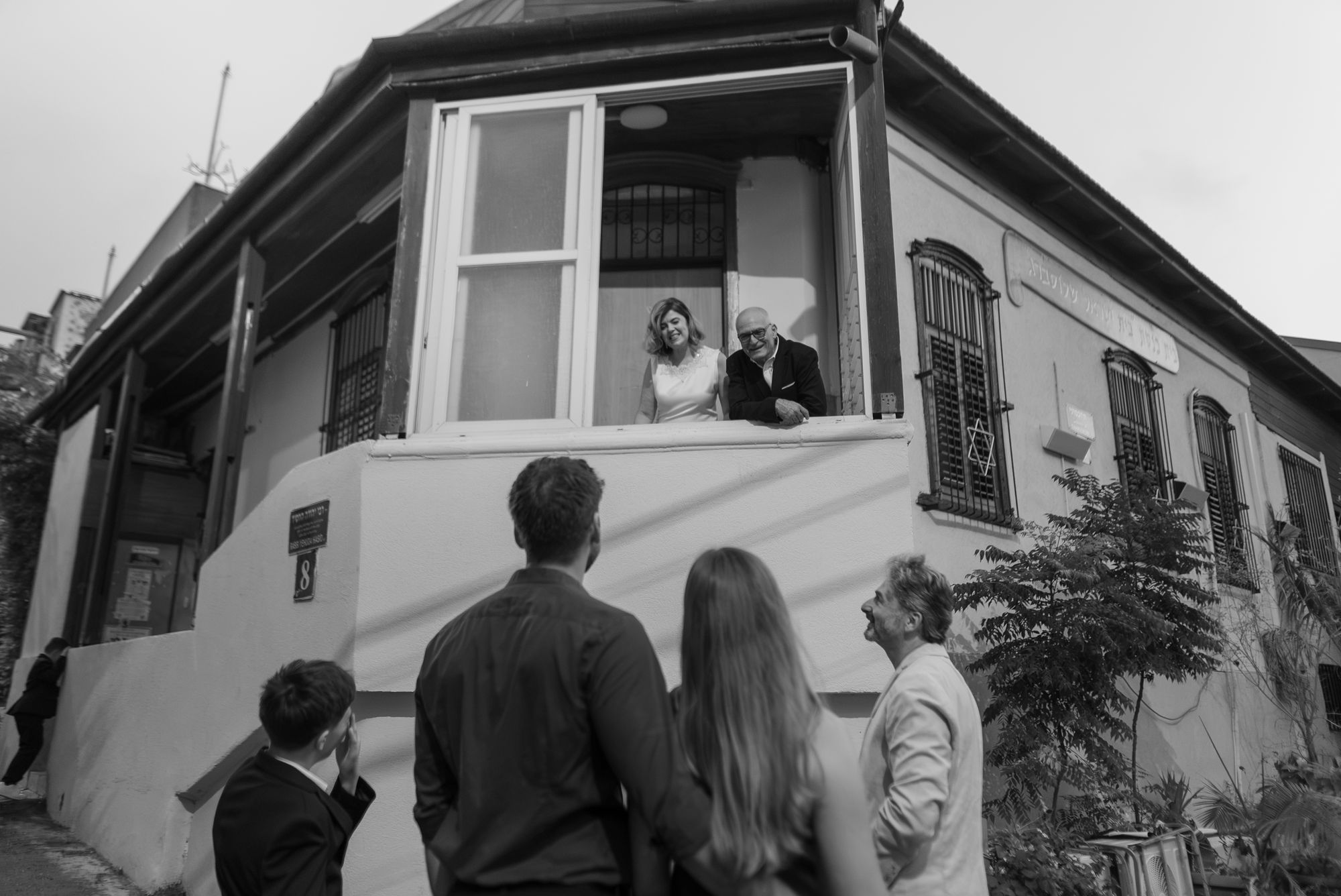 The couple leaning out of an open window as their family looks up from the street, black and white