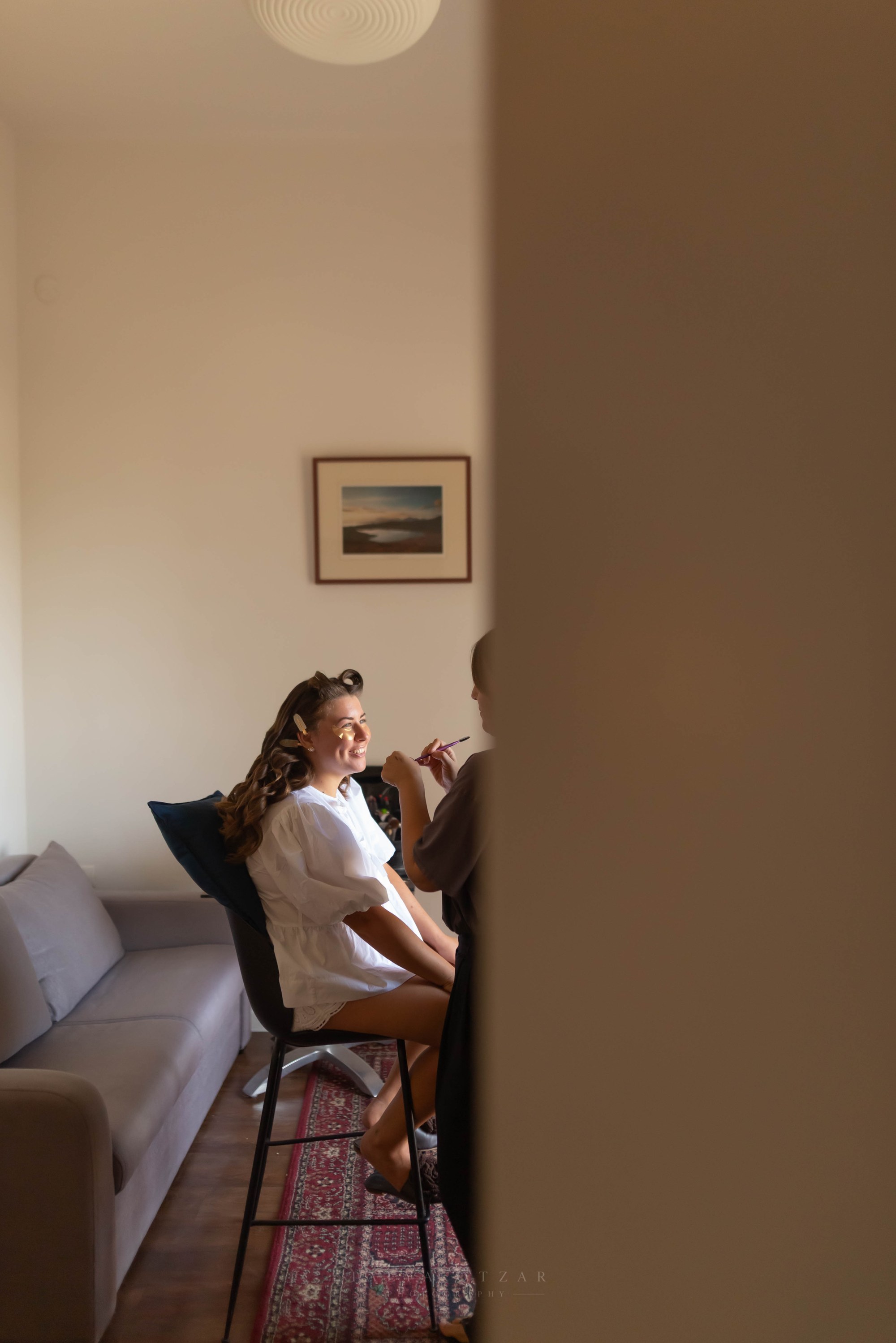 The bride smiling during her make-up, half hidden by the edge of a doorway