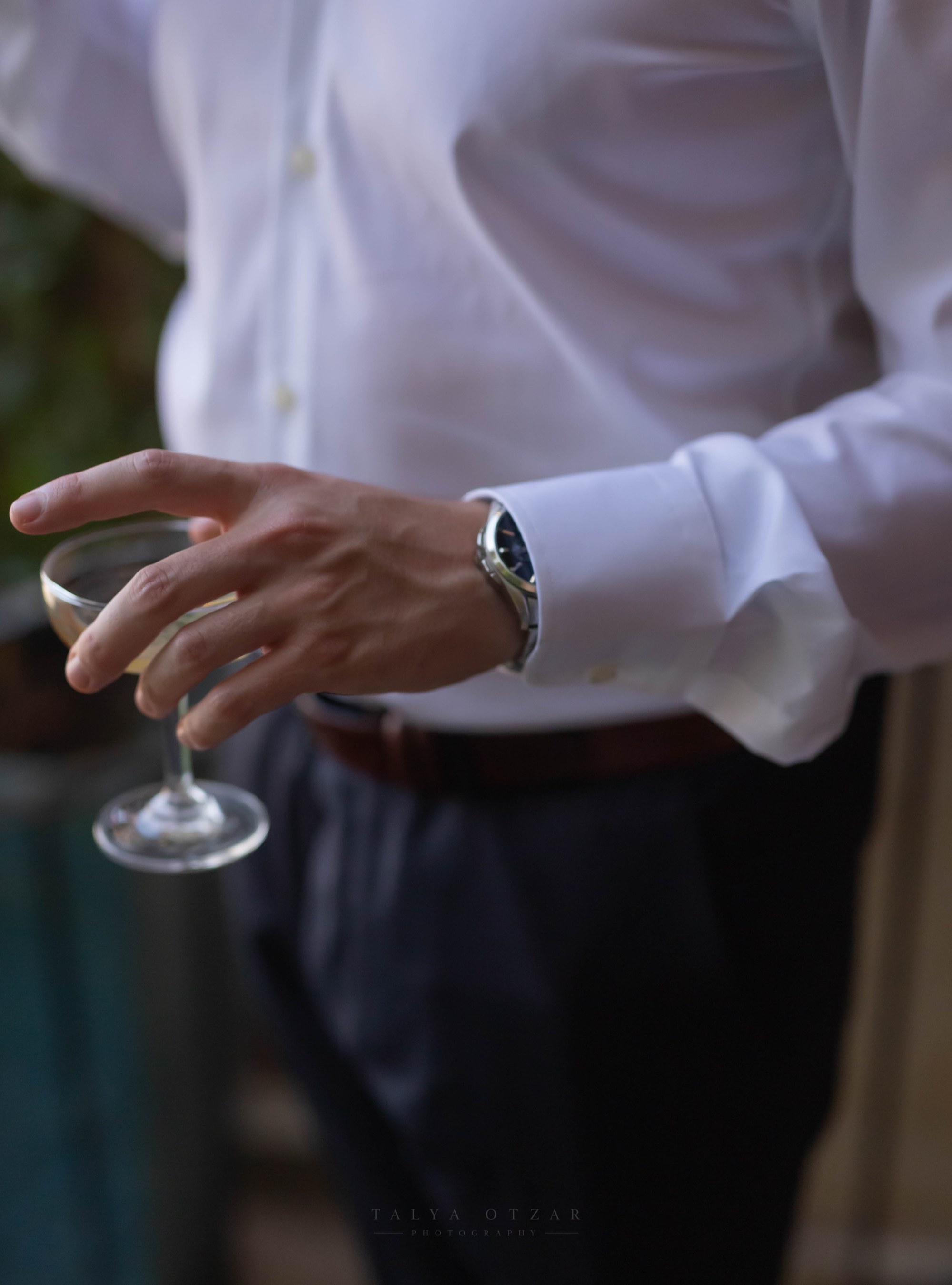 The groom holding a glass of wine, his watch catching the light