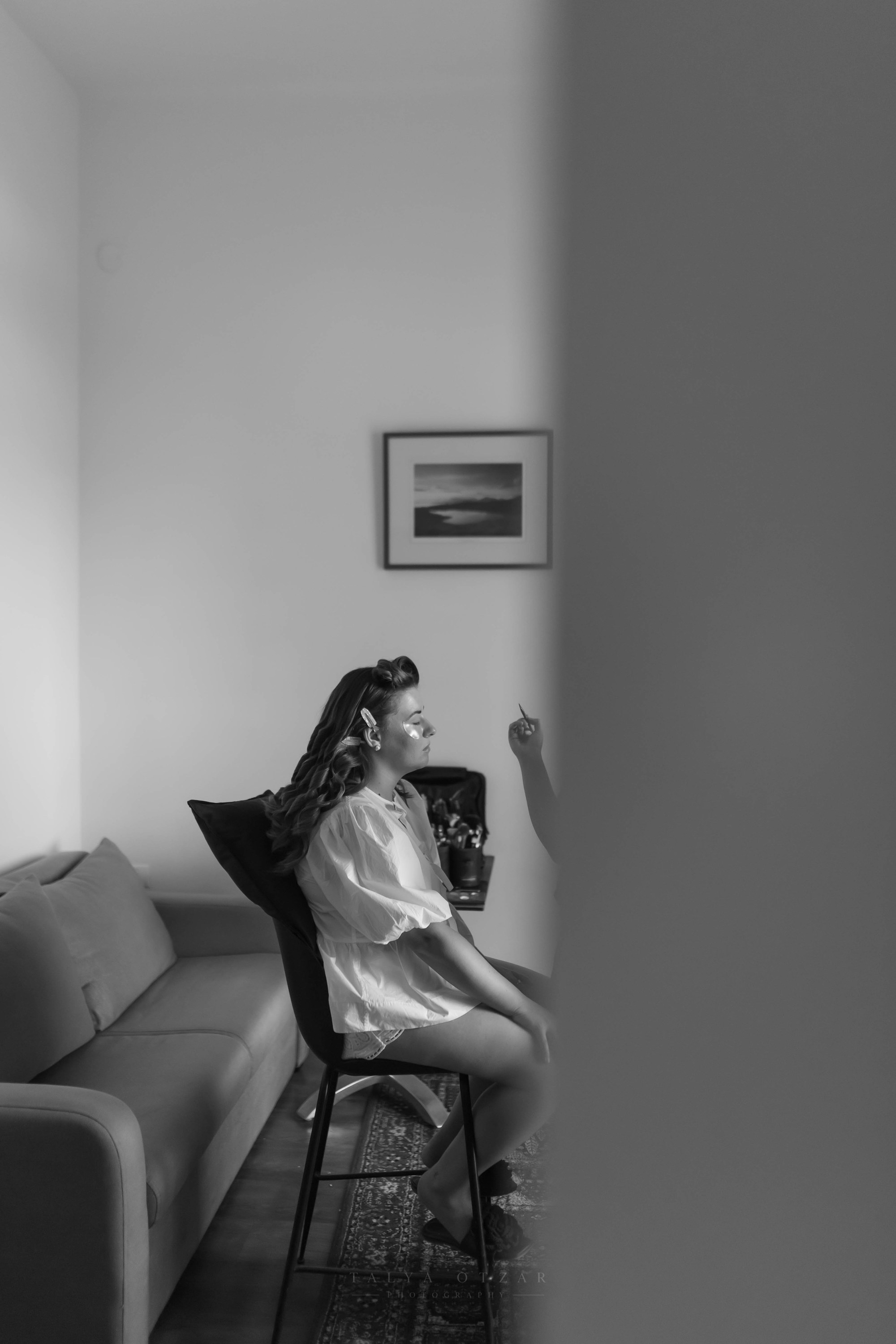 The bride on a tall chair by the sofa, seen through the doorway, black and white