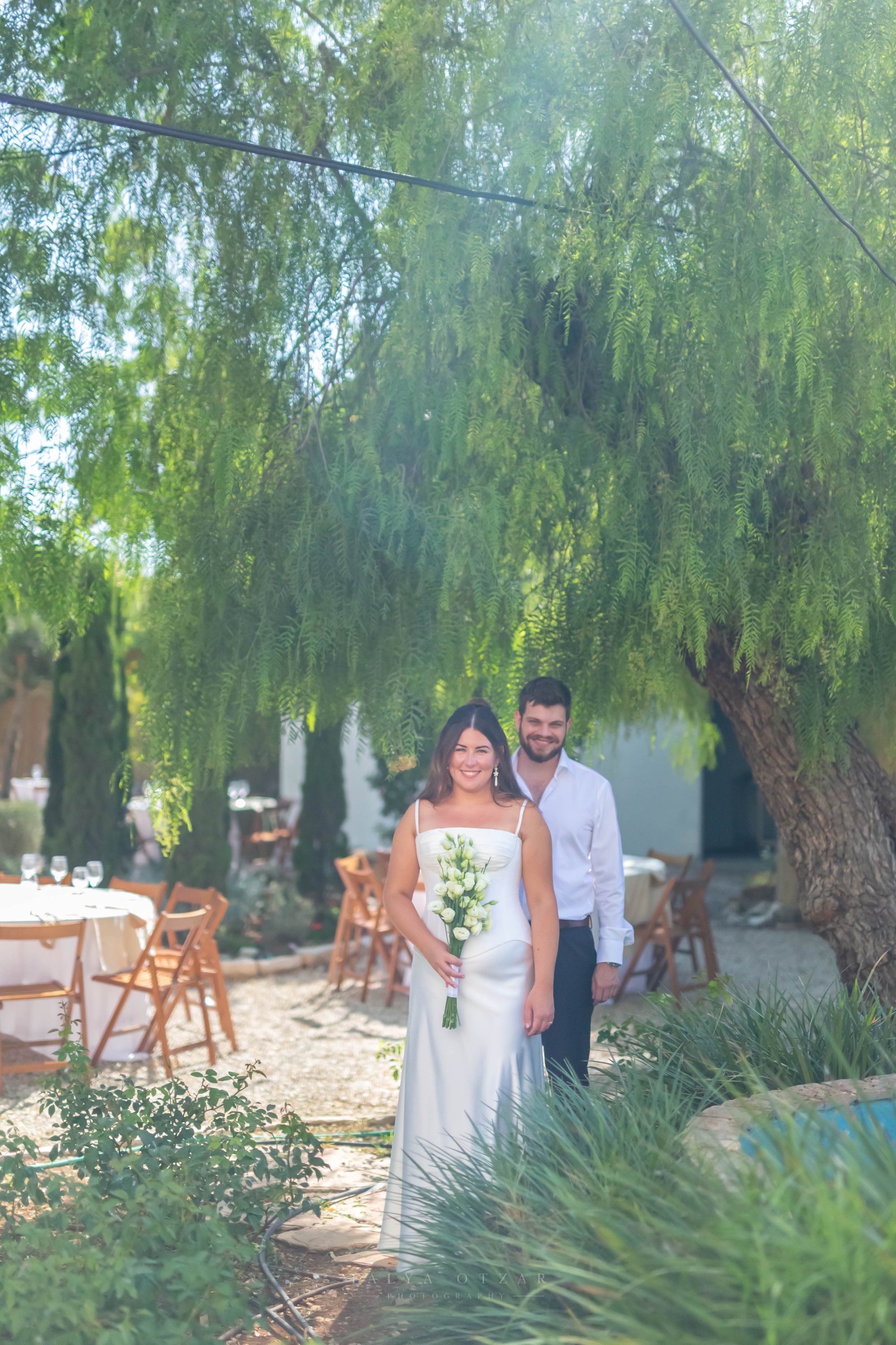 The couple standing on the garden path beneath a willowy tree