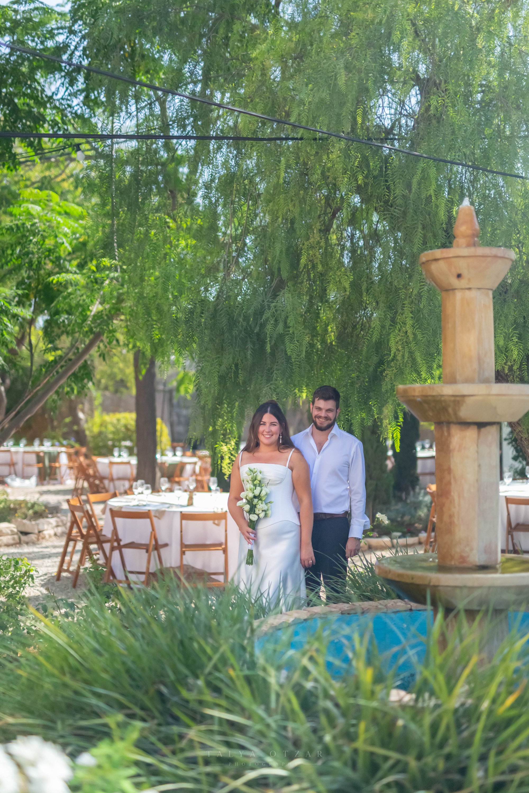 The couple beside the stone fountain among the garden tables