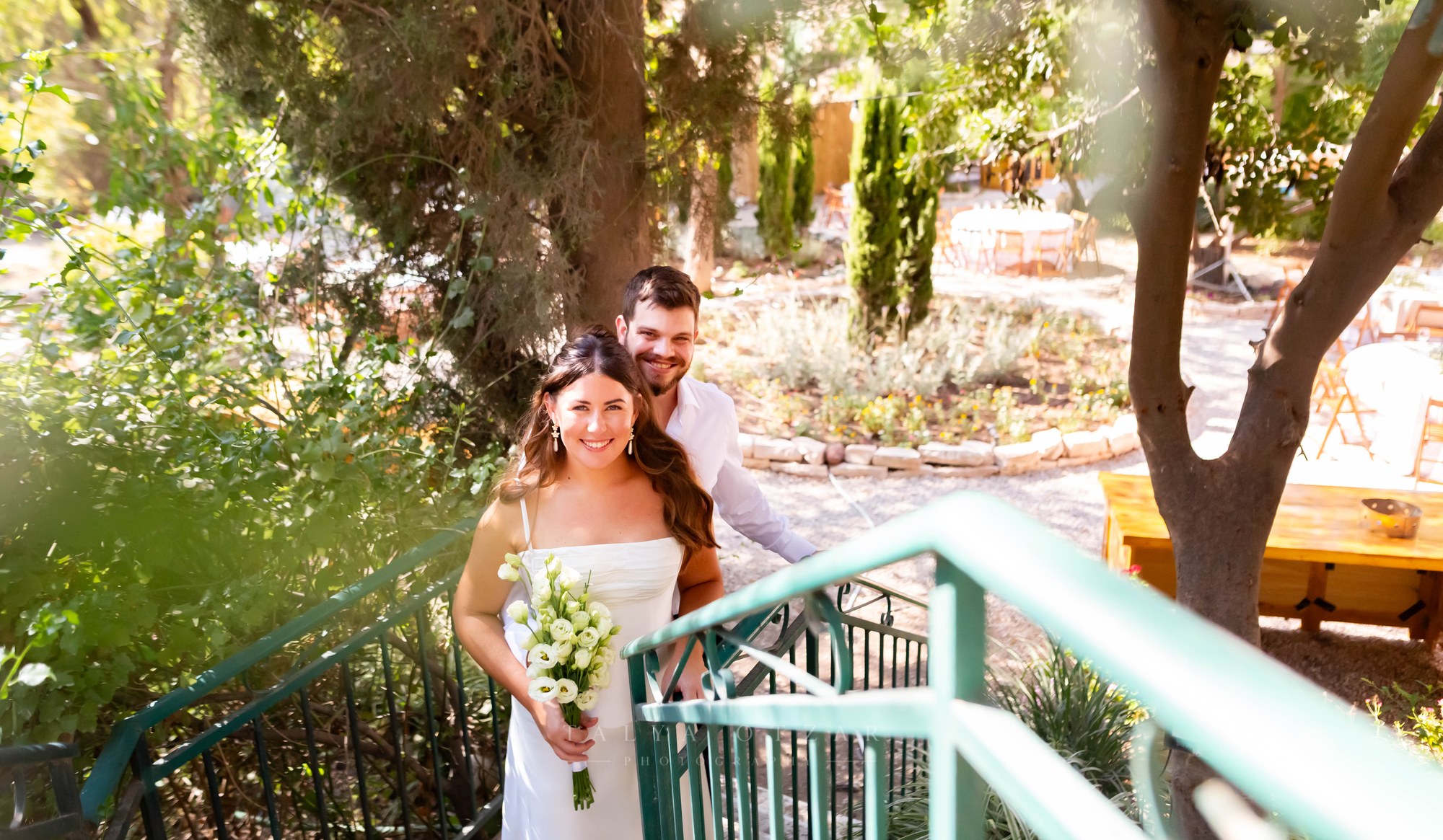 The couple on the green-railed garden steps, the bride holding her bouquet