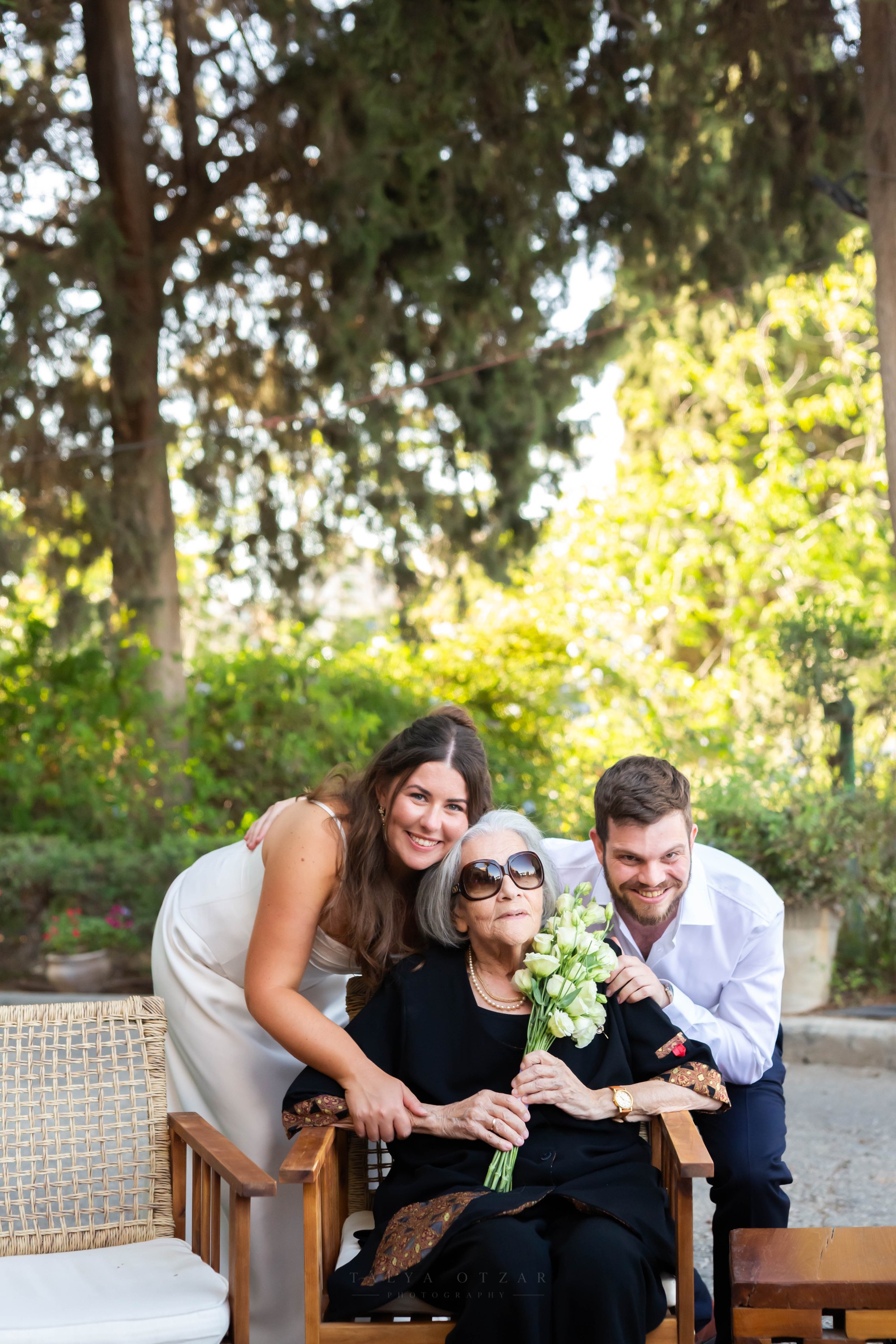 The couple embracing an elderly woman who holds the bouquet
