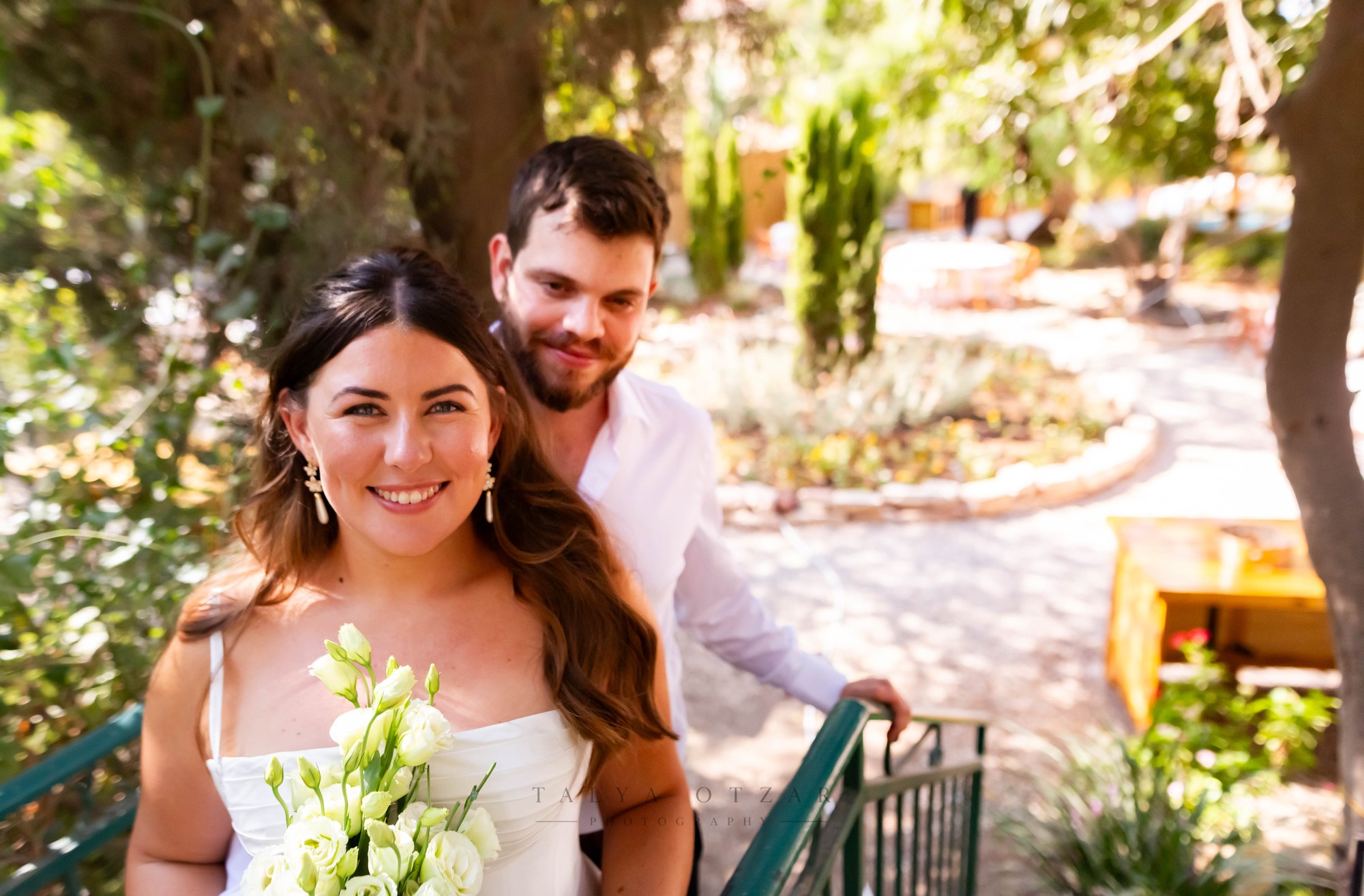 The bride and groom smiling at the top of the green-railed garden steps