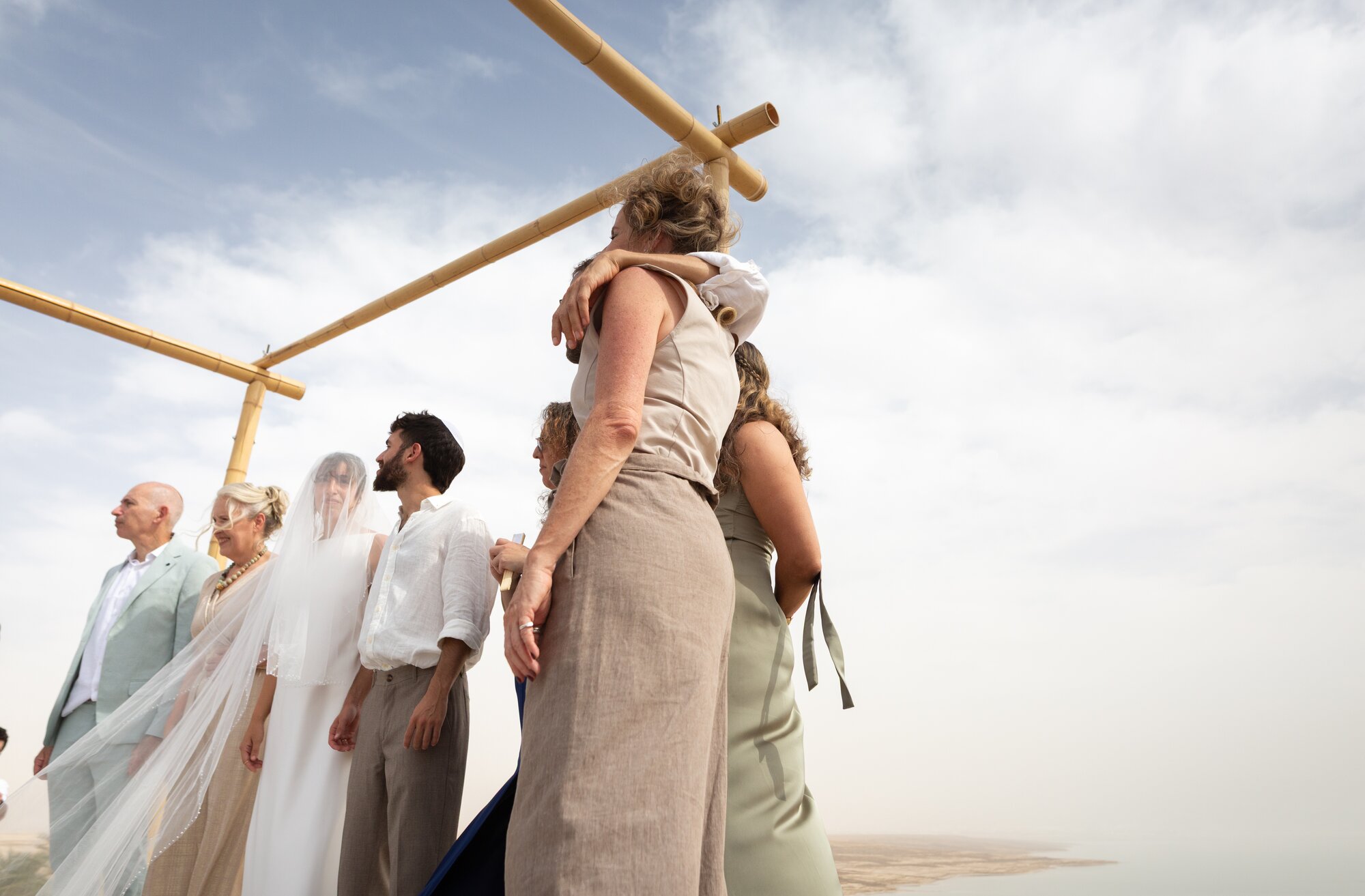 Family members embracing beside the bamboo chuppah under a wide desert sky