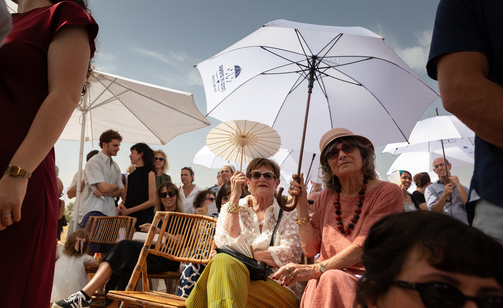 Guests seated under white umbrellas, smiling as the ceremony begins
