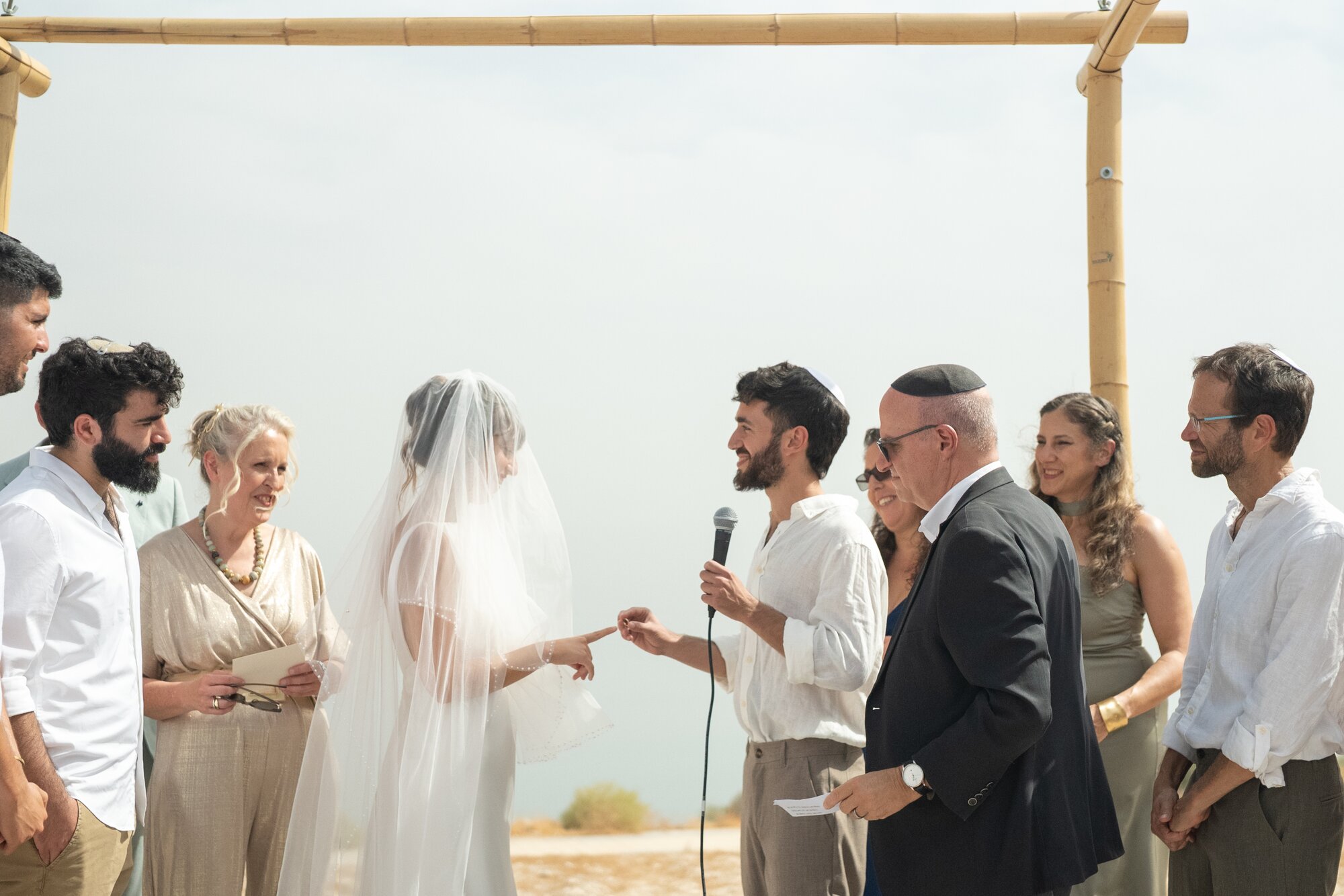 The couple under the chuppah during the ring exchange, the Dead Sea behind them