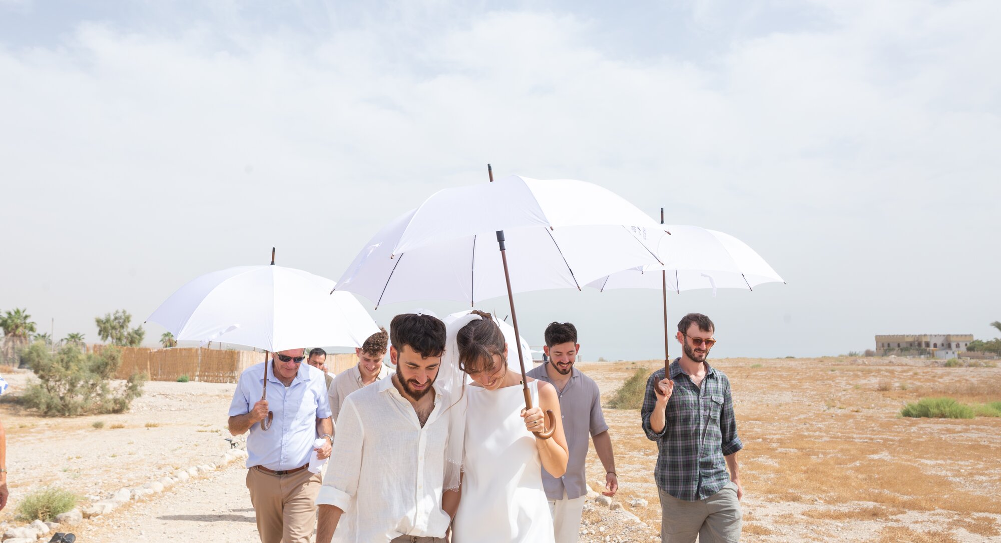 The couple and their friends crossing the desert under white umbrellas