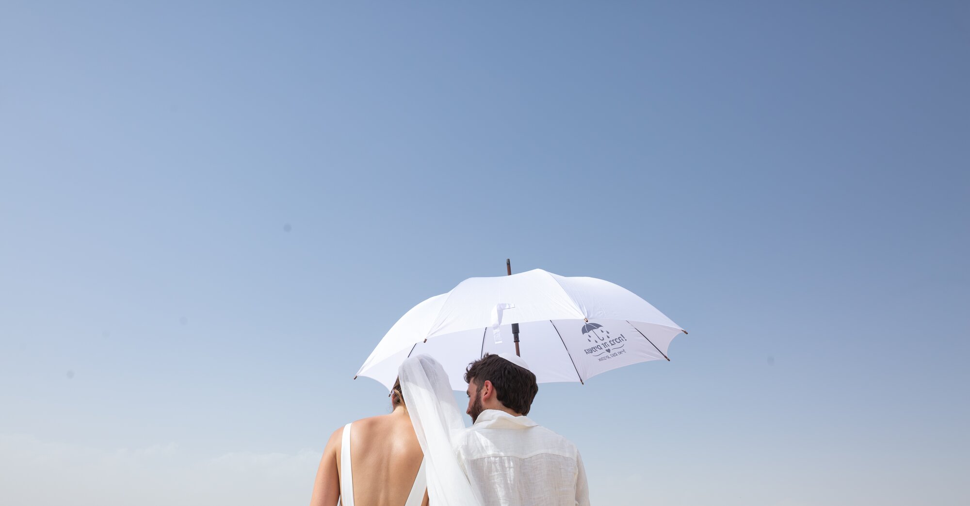 A white umbrella above the couple against a clear blue sky