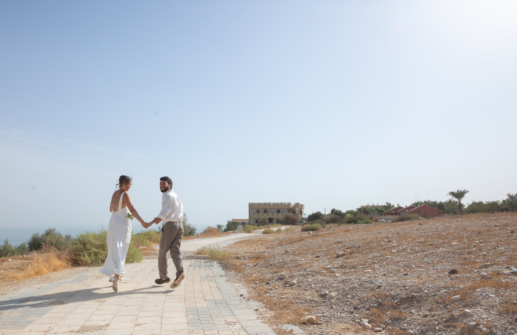 The couple walking hand in hand along a path above the sea