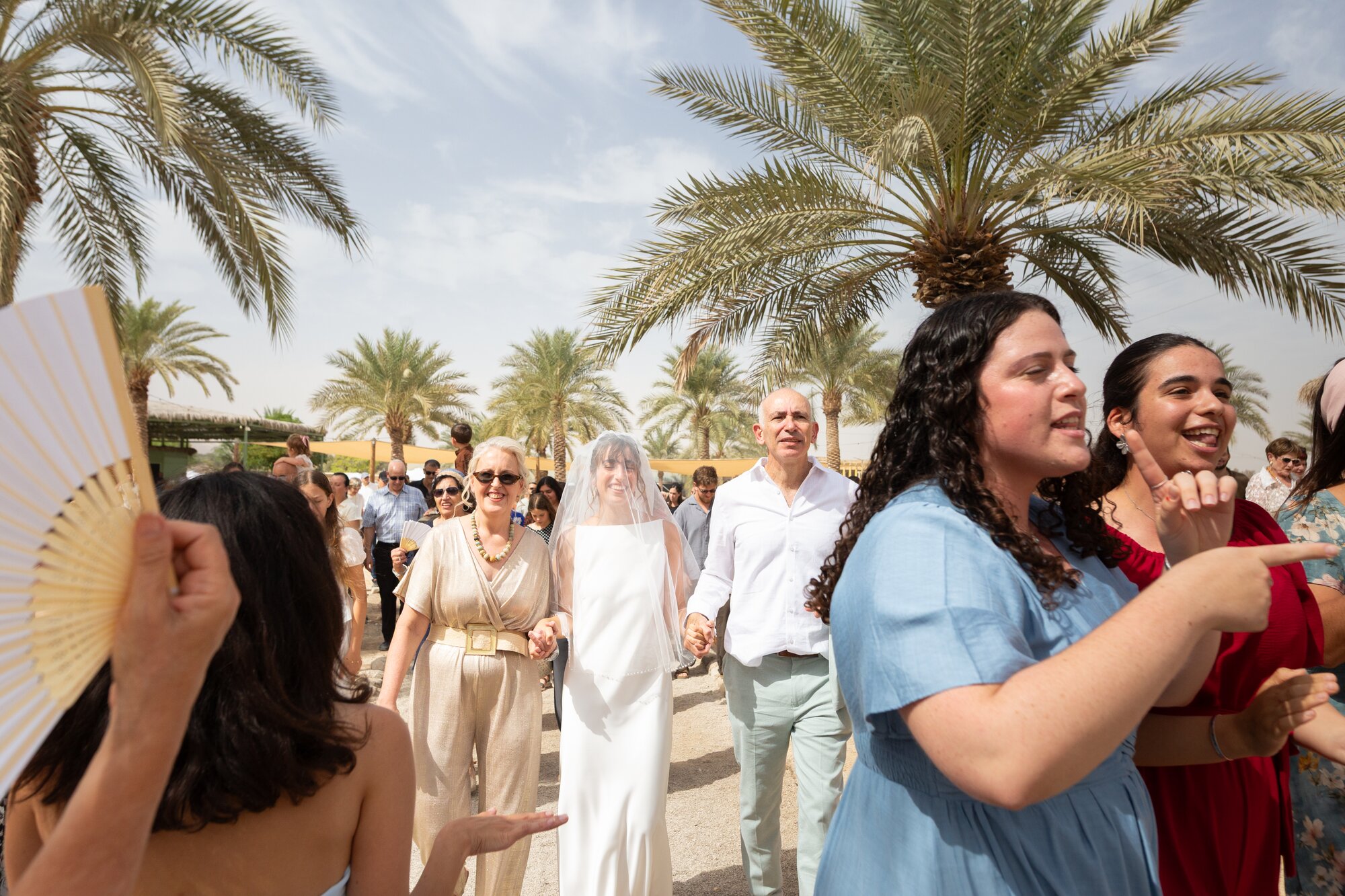 Guests singing and dancing as the bride arrives, palm trees behind them