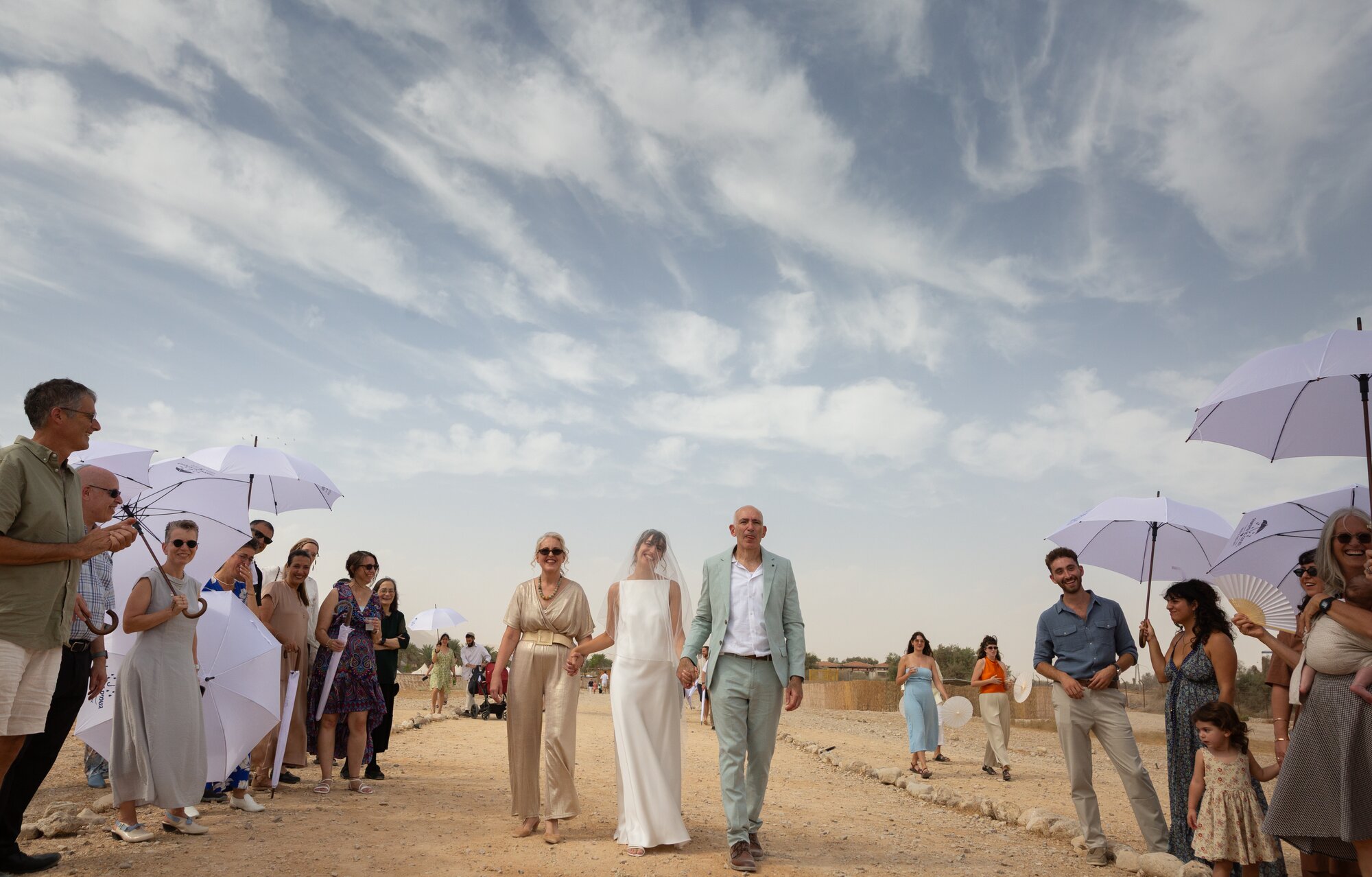 The bride walking toward the chuppah between her parents, guests on both sides